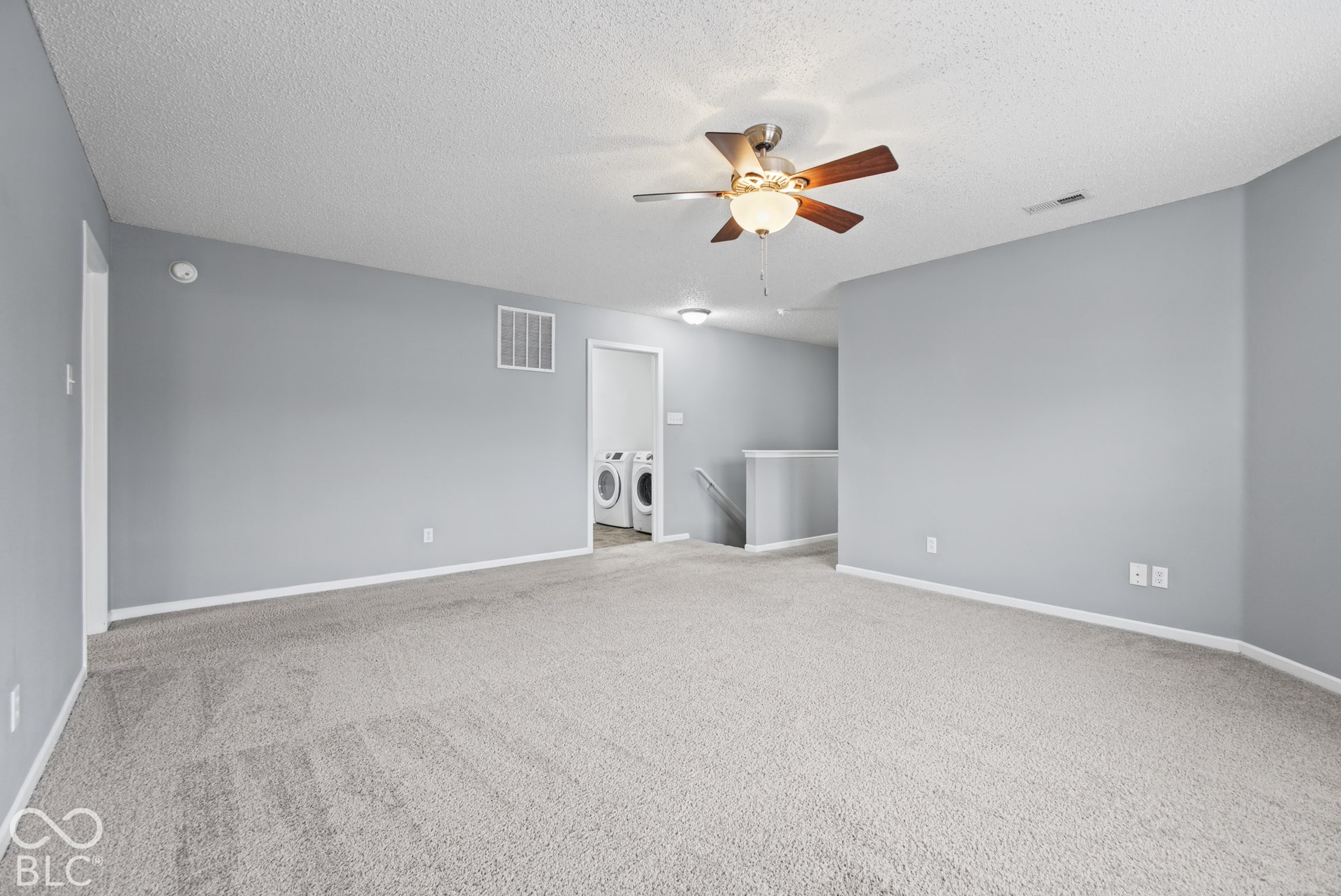 Open-concept interior featuring wall-to-wall carpeting, neutral-toned walls, and a ceiling fan with integrated lighting