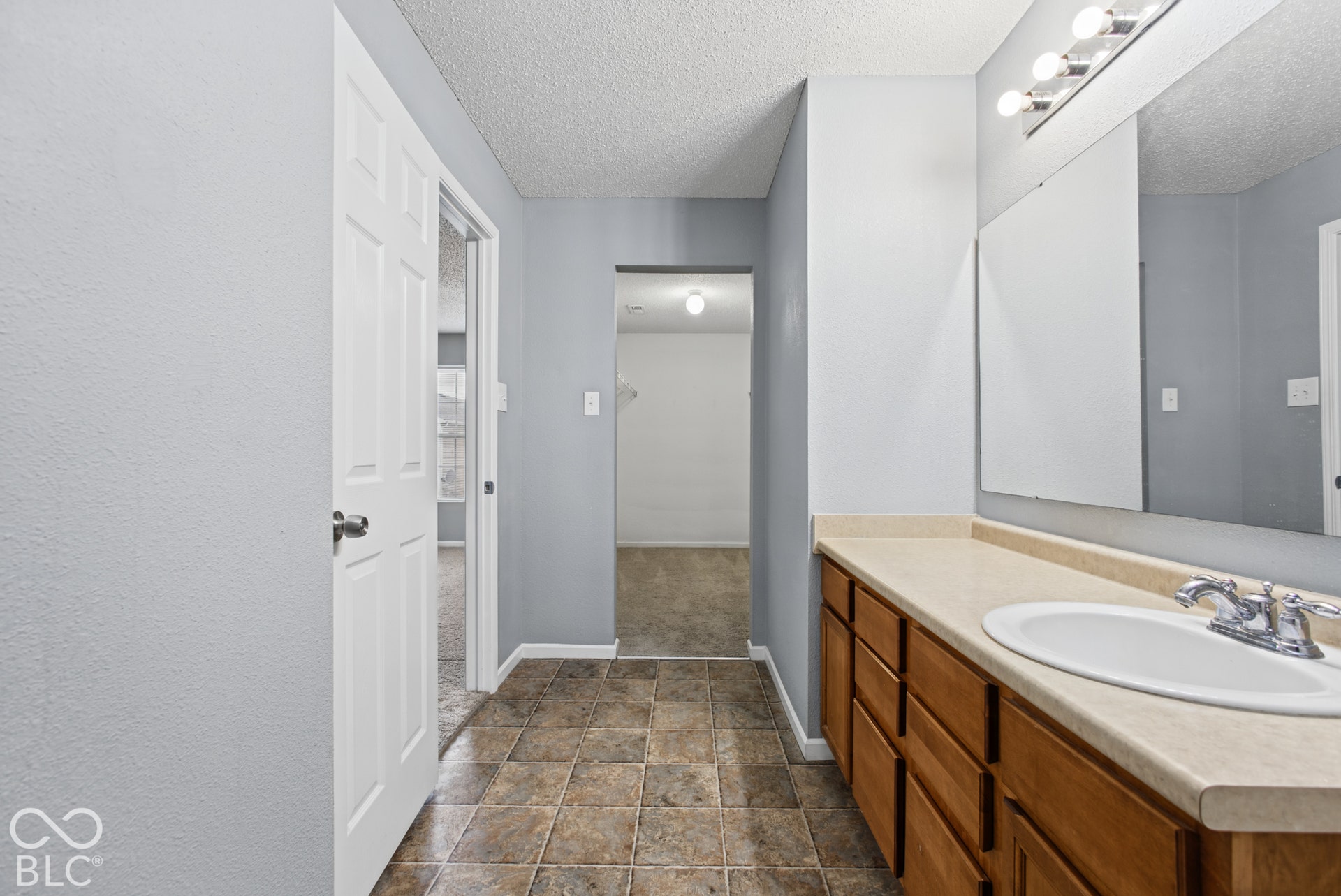 Bathroom featuring a wooden vanity with a solid-surface countertop, integrated oval sink, full-width wall mirror, and ceramic tile flooring