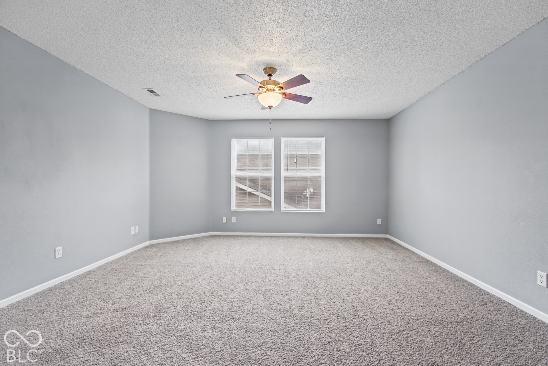 Spacious room featuring wall-to-wall carpeting, dual windows, and a central ceiling fan with integrated lighting