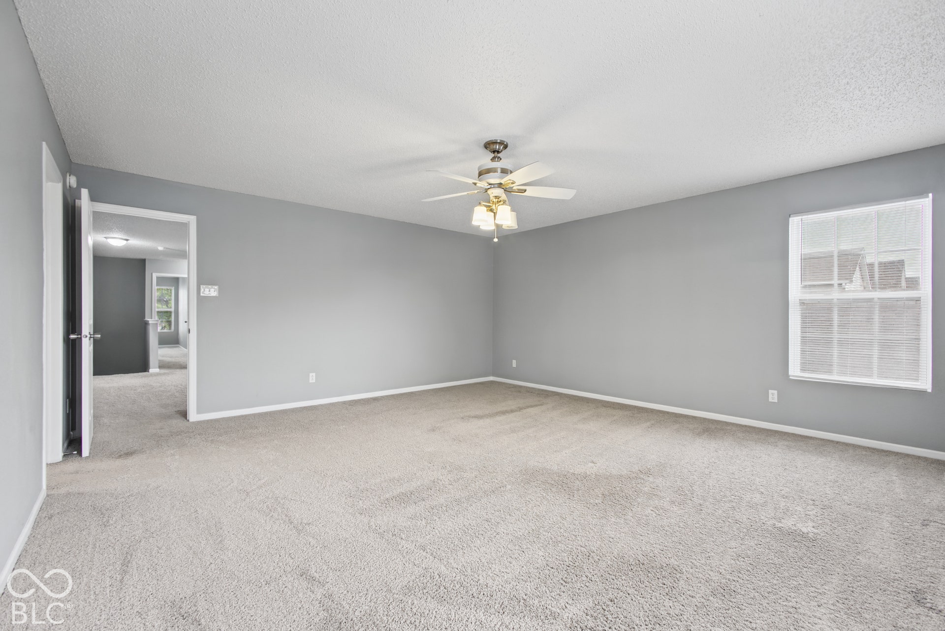 Spacious interior room featuring neutral wall paint, wall-to-wall carpeting, a central ceiling fan with integrated lighting, and a single-pane window