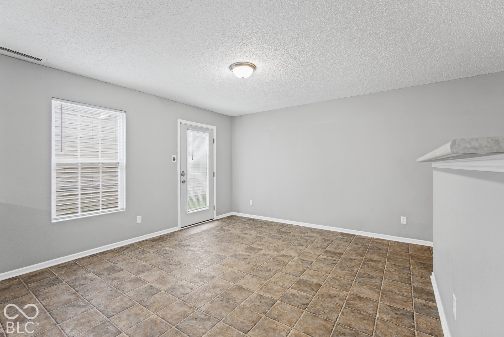 Neutral-toned room featuring tile flooring, a single-hung window, a glass-panel exterior door, and flush-mount ceiling lighting