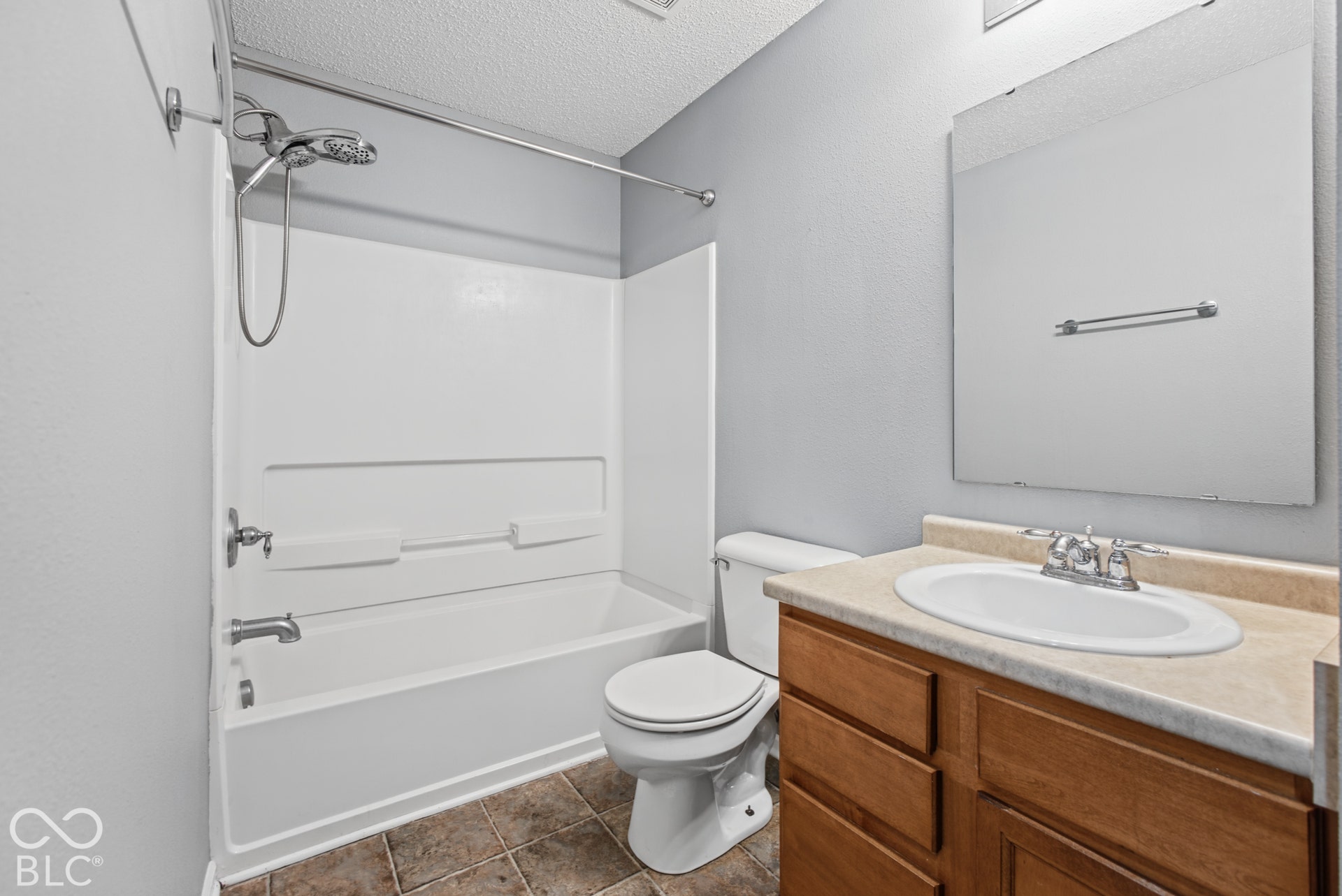 Bathroom featuring a wood-finish vanity with a stone-composite countertop, integrated sink, tub-shower combination, and wall-mounted mirror