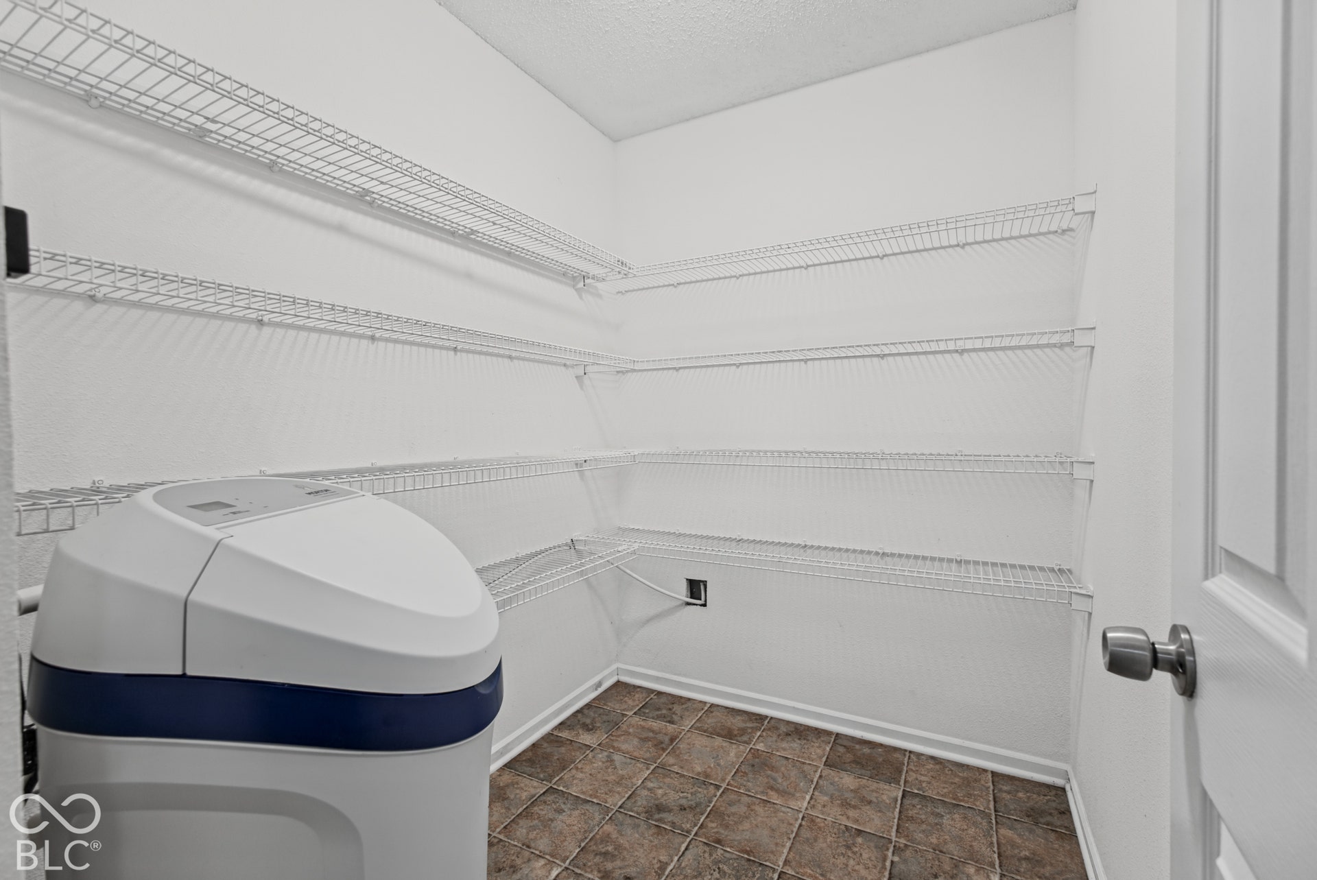 Storage area featuring white wire shelving, tiled flooring, and a water softening system