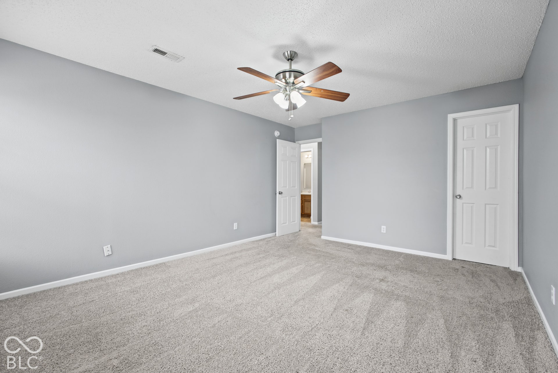 Neutral-toned carpeted flooring, multi-panel interior doors, and a ceiling-mounted fan with integrated light fixture