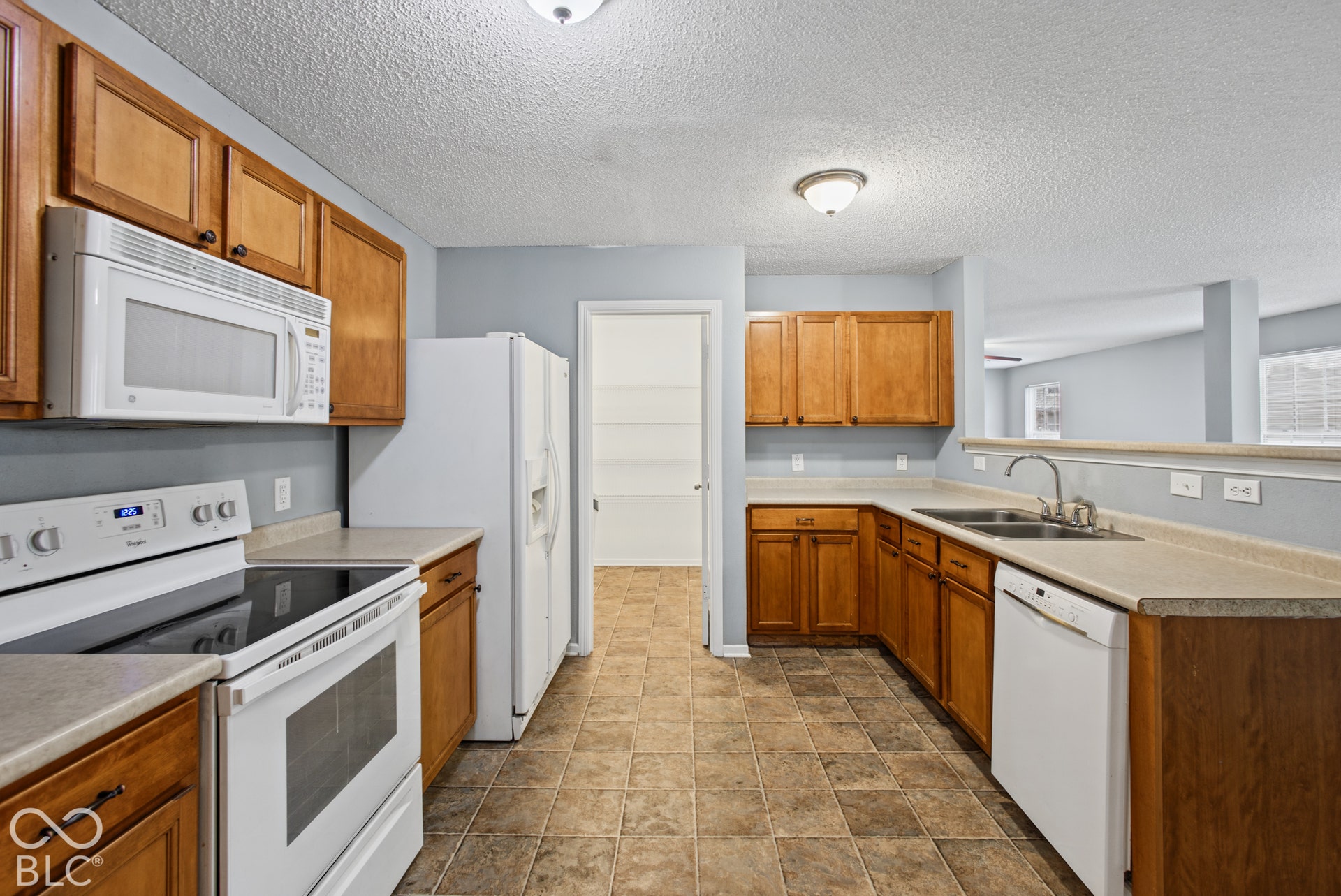 Kitchen featuring medium-tone wood cabinetry, laminate countertops, a double-basin stainless steel sink, built-in white appliances, and tile flooring