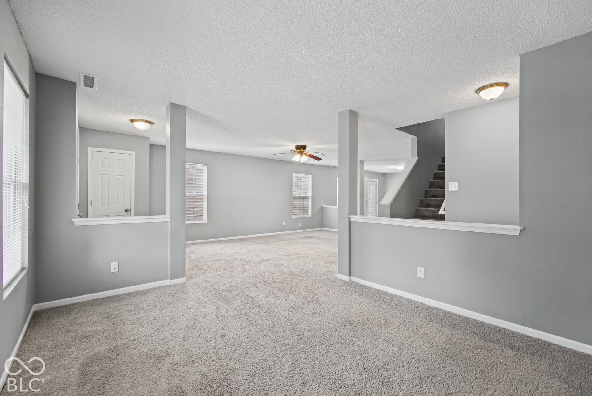 Open-concept interior featuring neutral wall tones, wall-to-wall carpeting, multiple structural partition walls, ceiling-mounted light fixtures, and a staircase with carpeted treads