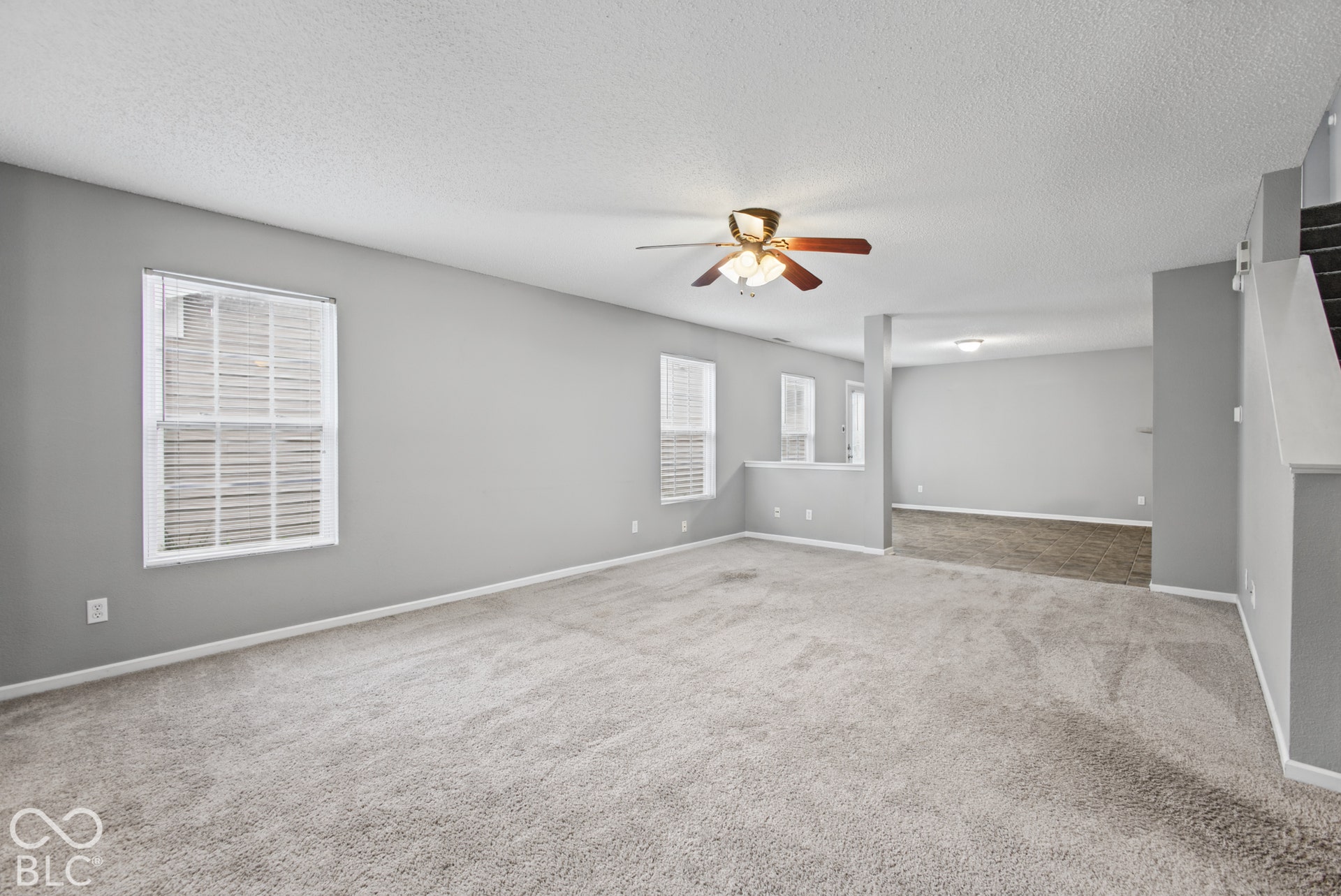 Neutral-toned interior featuring wall-to-wall carpeting, multiple windows with horizontal blinds, and a centrally mounted ceiling fan with integrated lighting