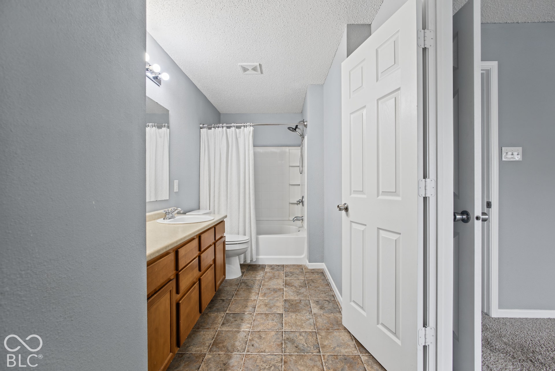 Bathroom featuring a wood-tone vanity, solid-surface countertop with an integrated basin, tile flooring, and a shower-tub combination with a wall-mounted faucet