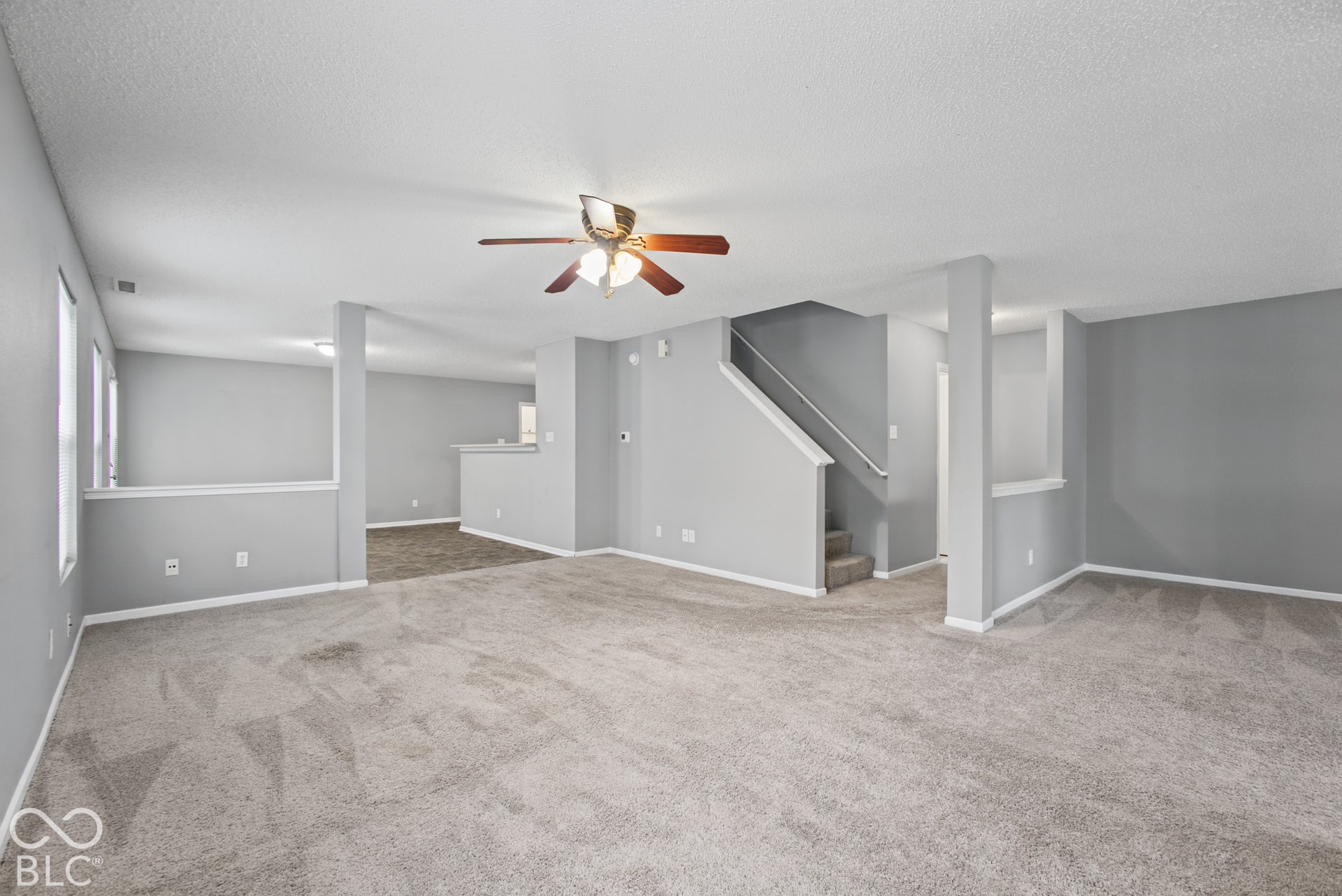Neutral wall-to-wall carpeting, ceiling fan with light fixture, staircase with metal railing, and neutral wall paint
