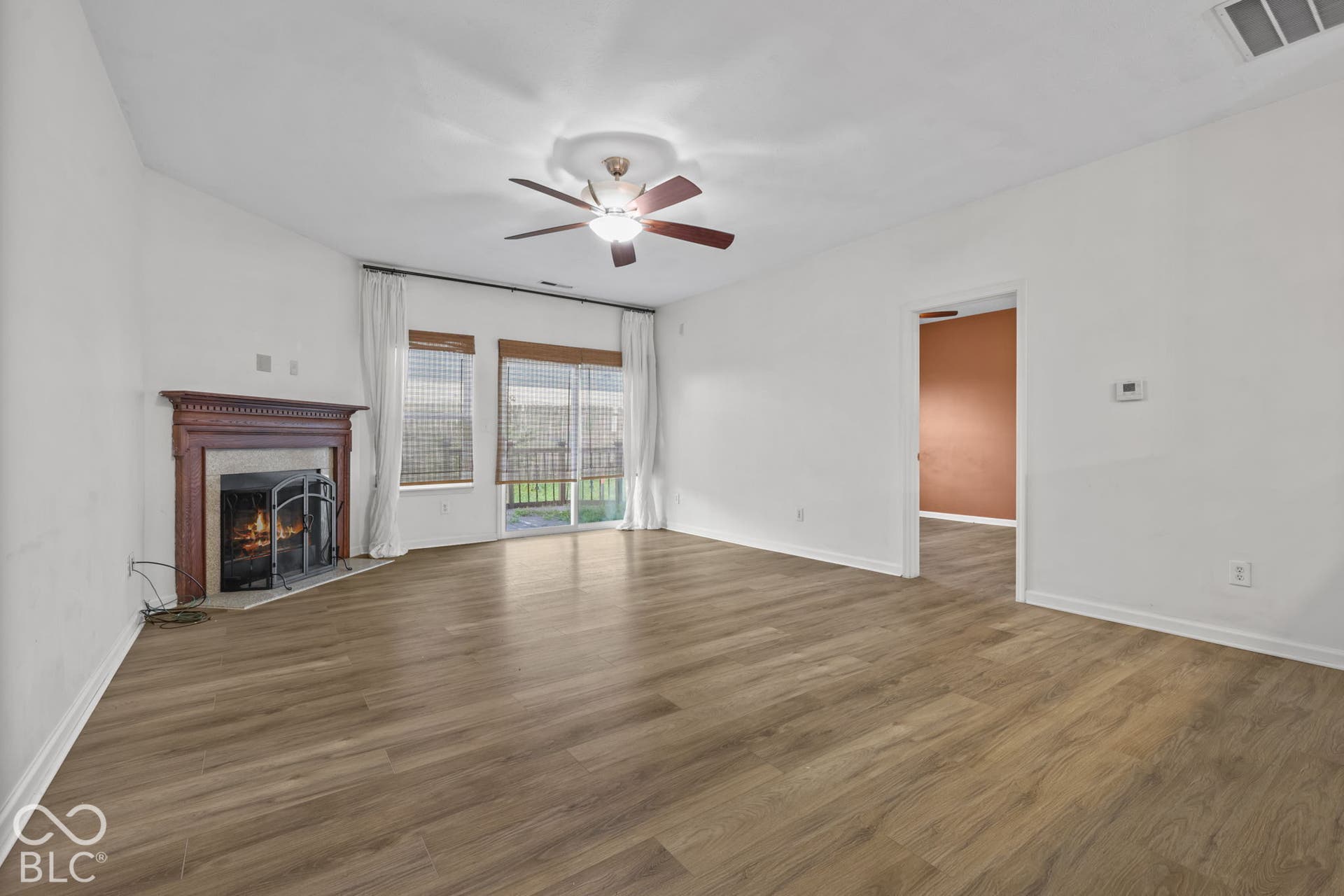 Living area featuring wood-finish flooring, a fireplace with a decorative mantel, sliding glass doors, and a ceiling fan
