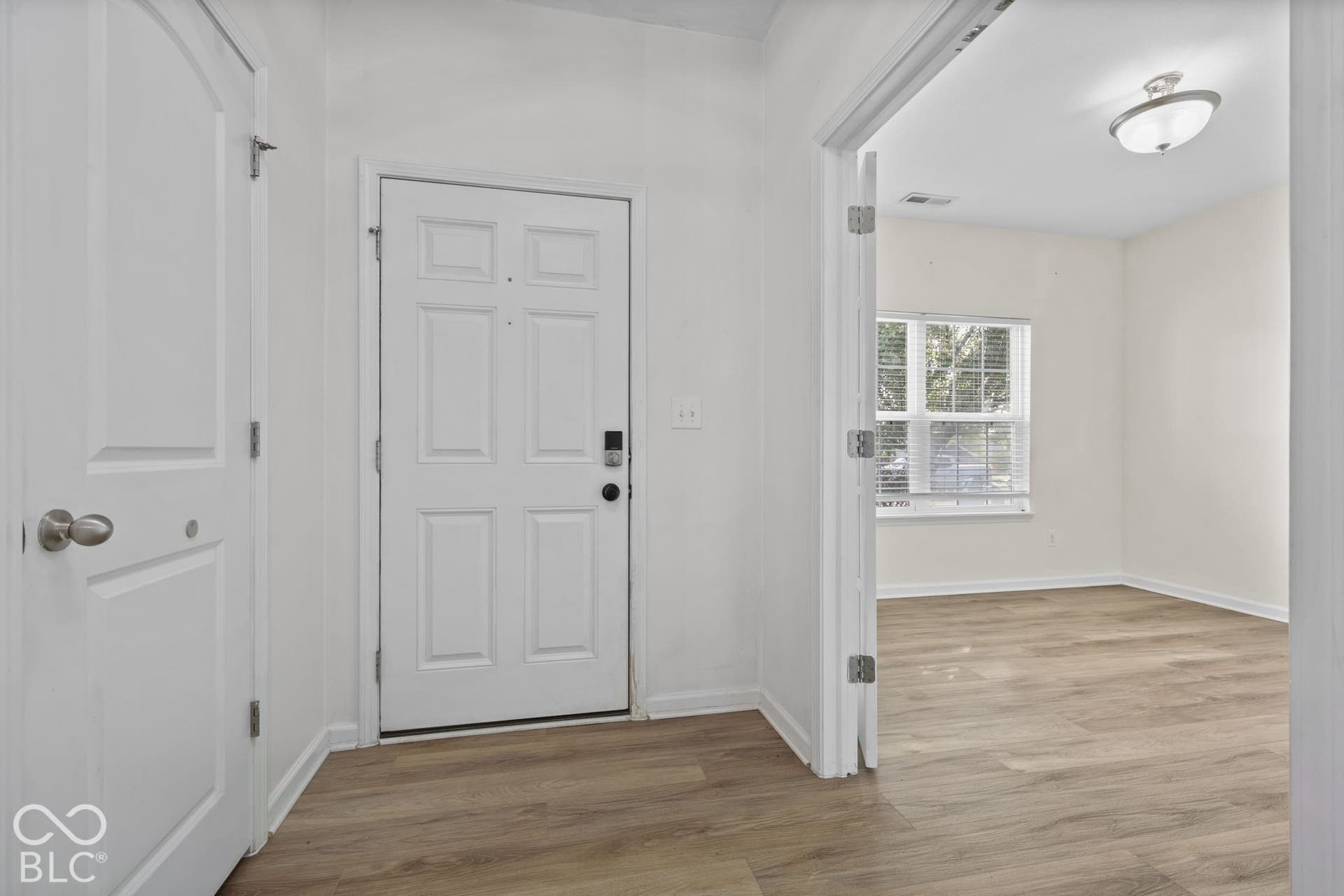 Entryway featuring wood-finish flooring, a six-panel door, interior swing doors, and a flush-mount ceiling light fixture