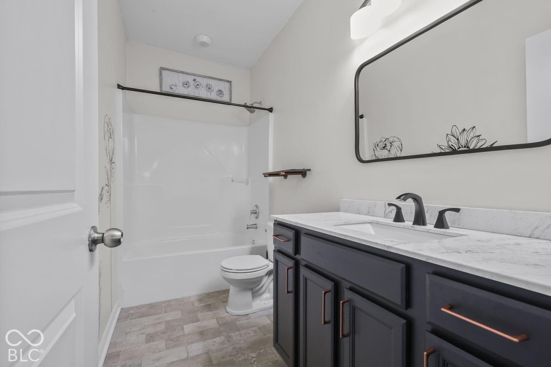 Modern primary bathroom featuring a dark cabinetry vanity with marble countertop, matte black faucet and hardware, and a framed black-trimmed mirror