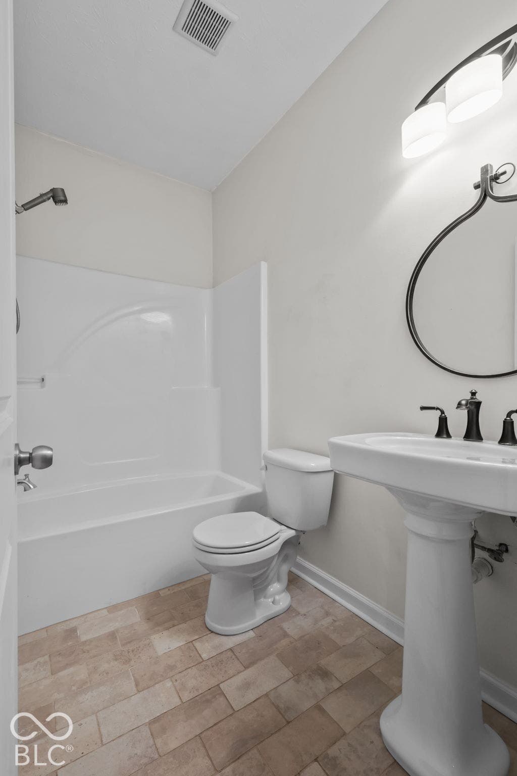 Bathroom featuring a pedestal sink, multi-light vanity fixture, circular wall mirror, and a tub-shower combination with tile-finish flooring