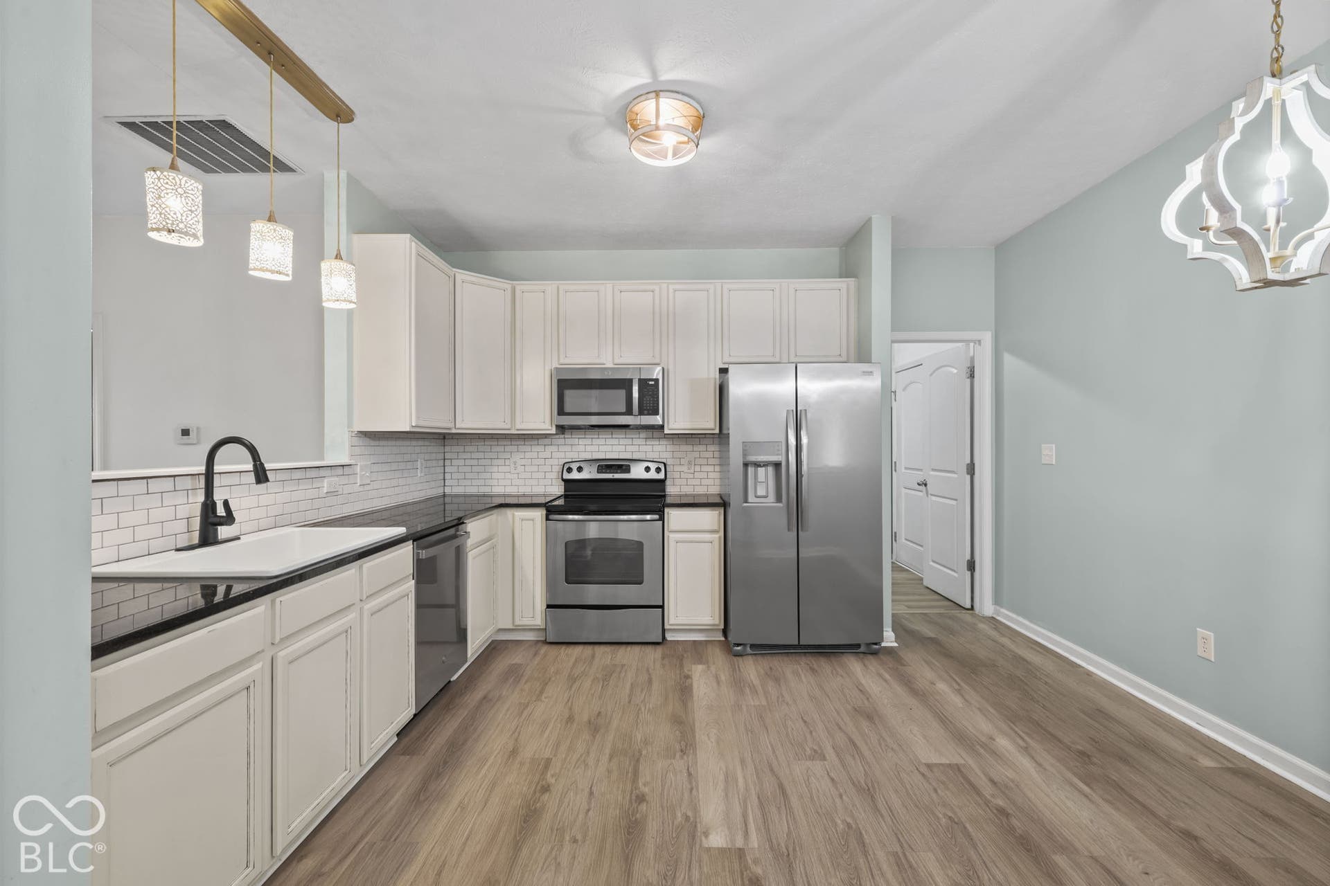 Kitchen featuring white shaker cabinetry, dark countertops, white subway tile backsplash, stainless steel appliances, and wood-finish flooring