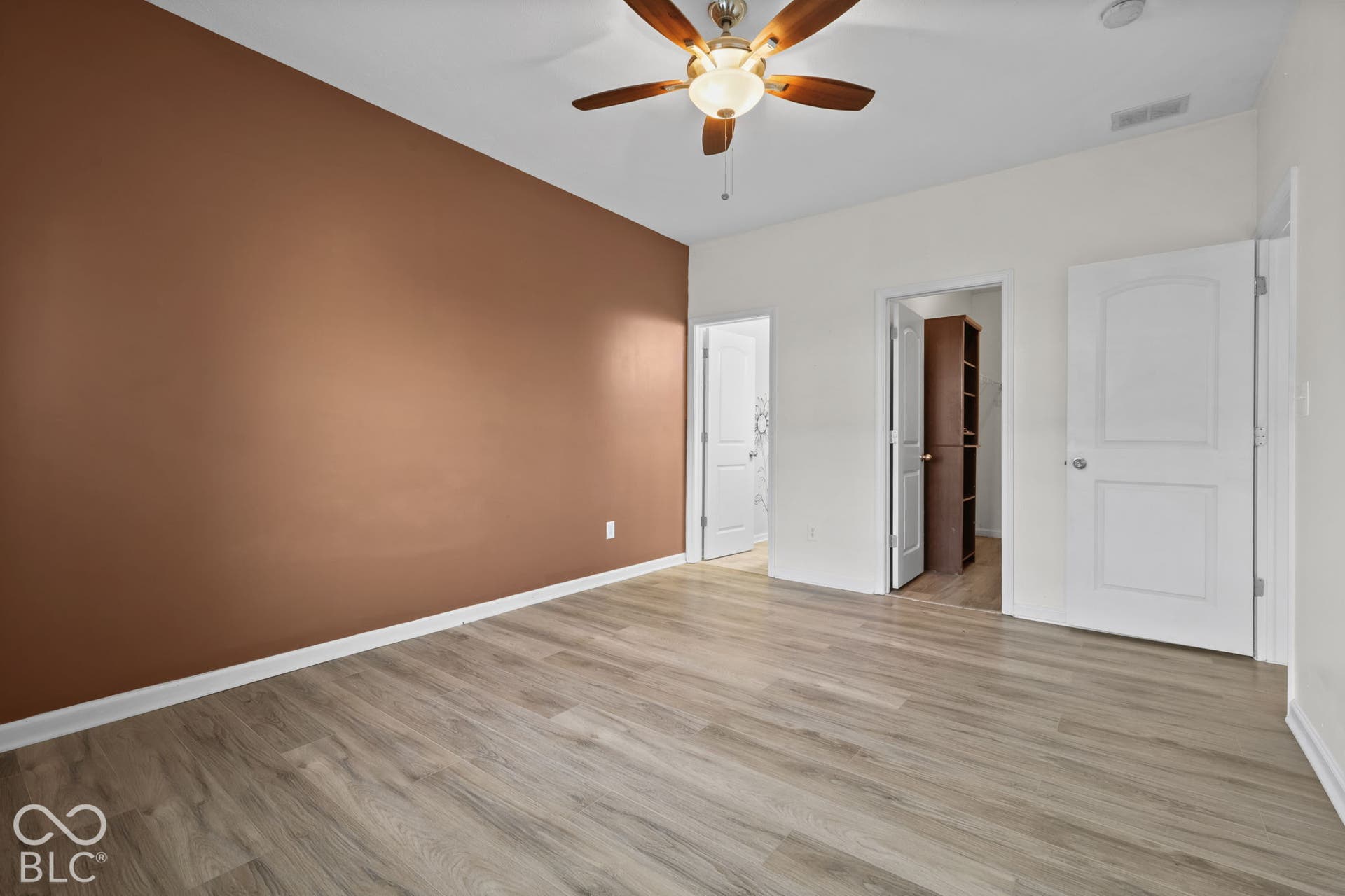 Wood-finish flooring, ceiling fan with integrated lighting, and solid-core interior doors with arched-panel detailing