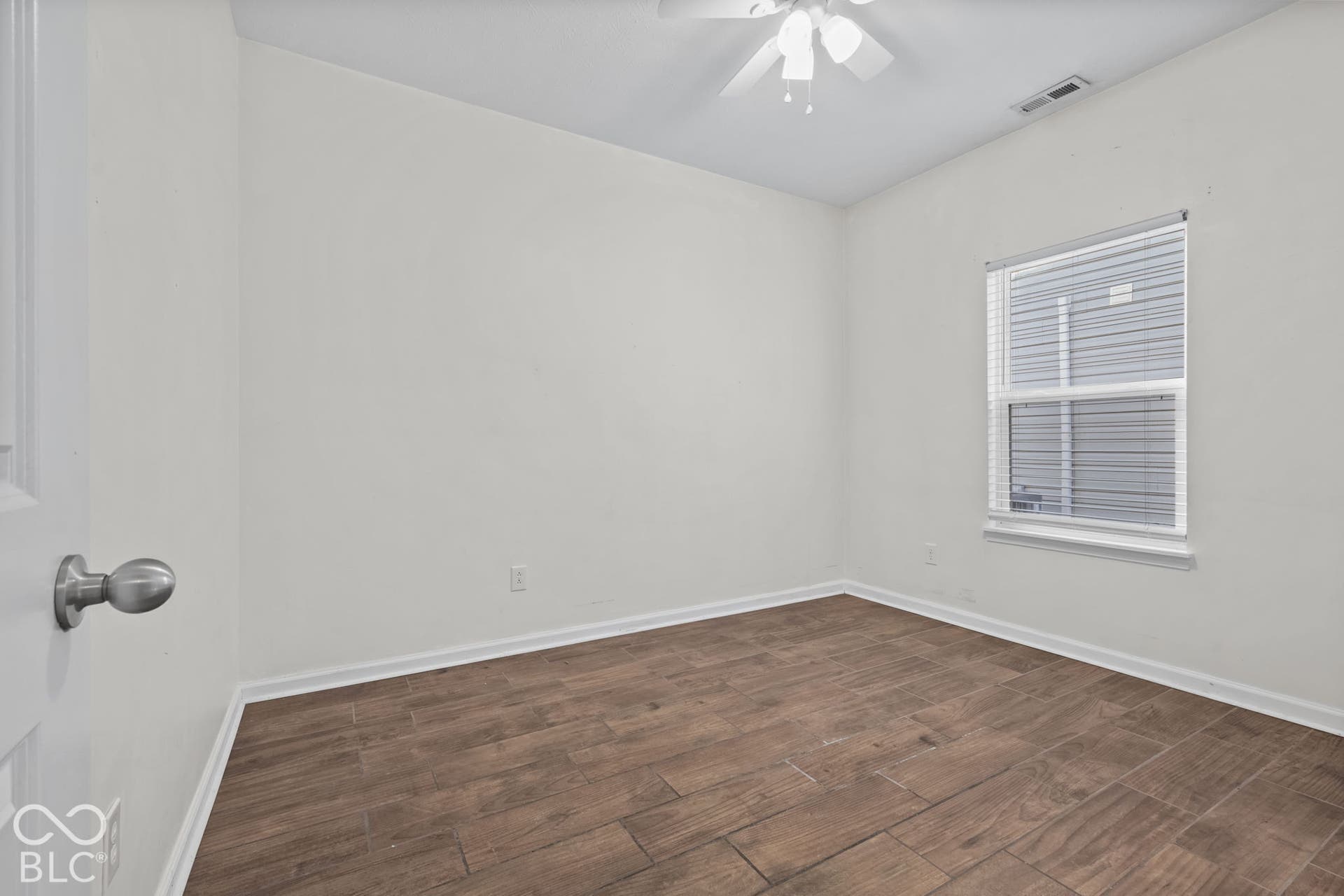 Neutral-toned room featuring wood-finish flooring, a ceiling fan with integrated lighting, and a window with horizontal blinds