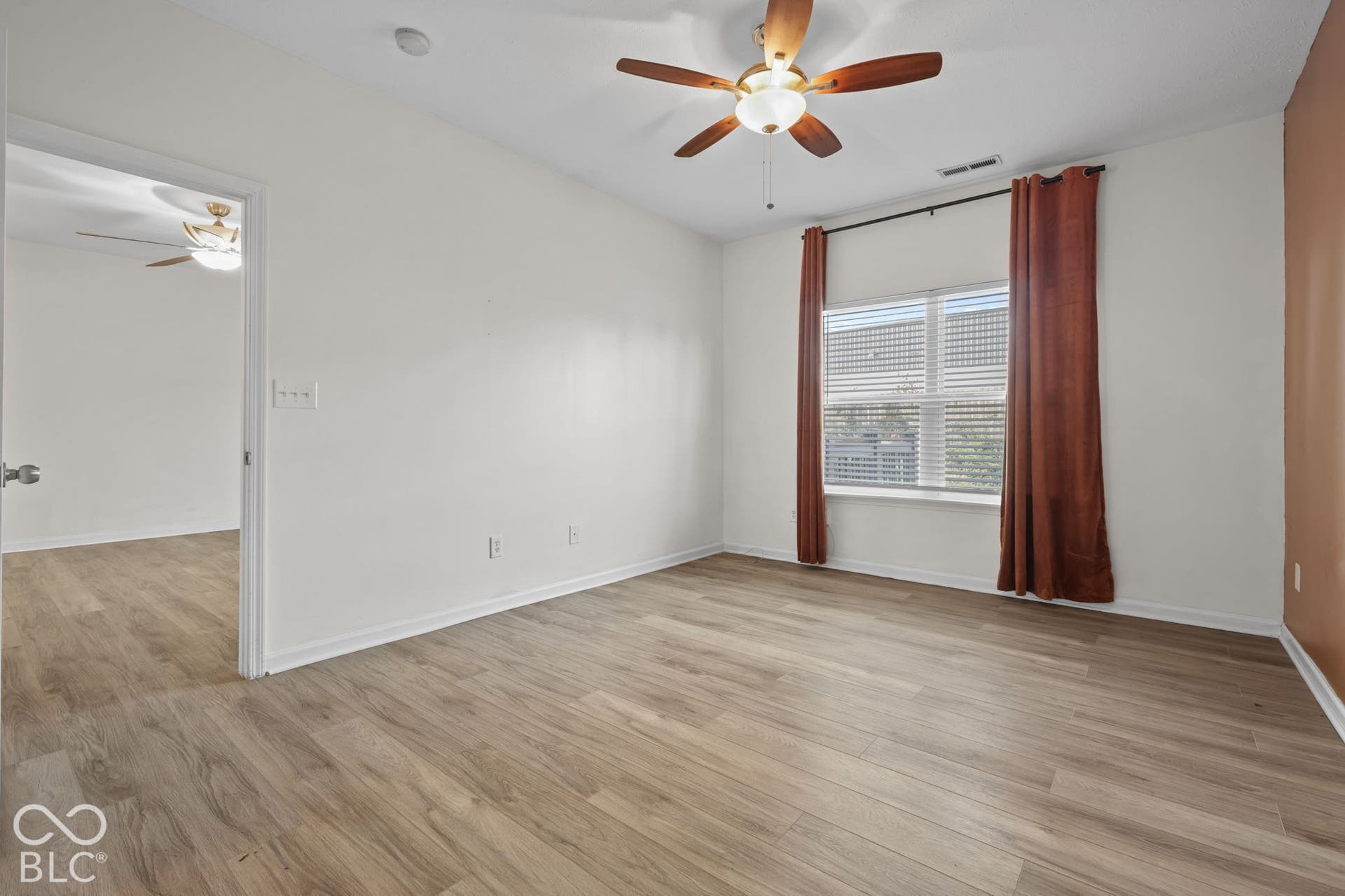 Room featuring wood-finish flooring, a ceiling fan with integrated lighting, and a window with horizontal blinds