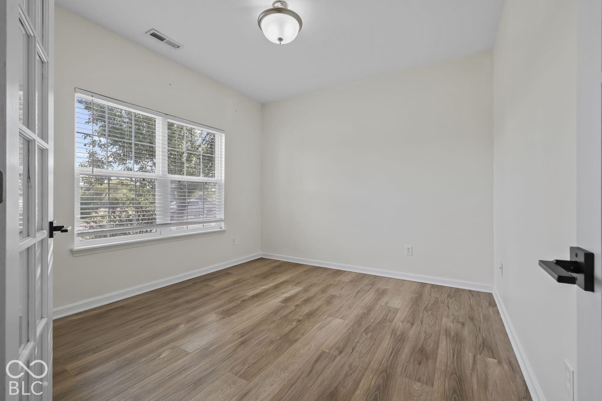 Room featuring wood-finish flooring, a multi-pane French door entry, a flush-mount ceiling light fixture, and horizontal window blinds