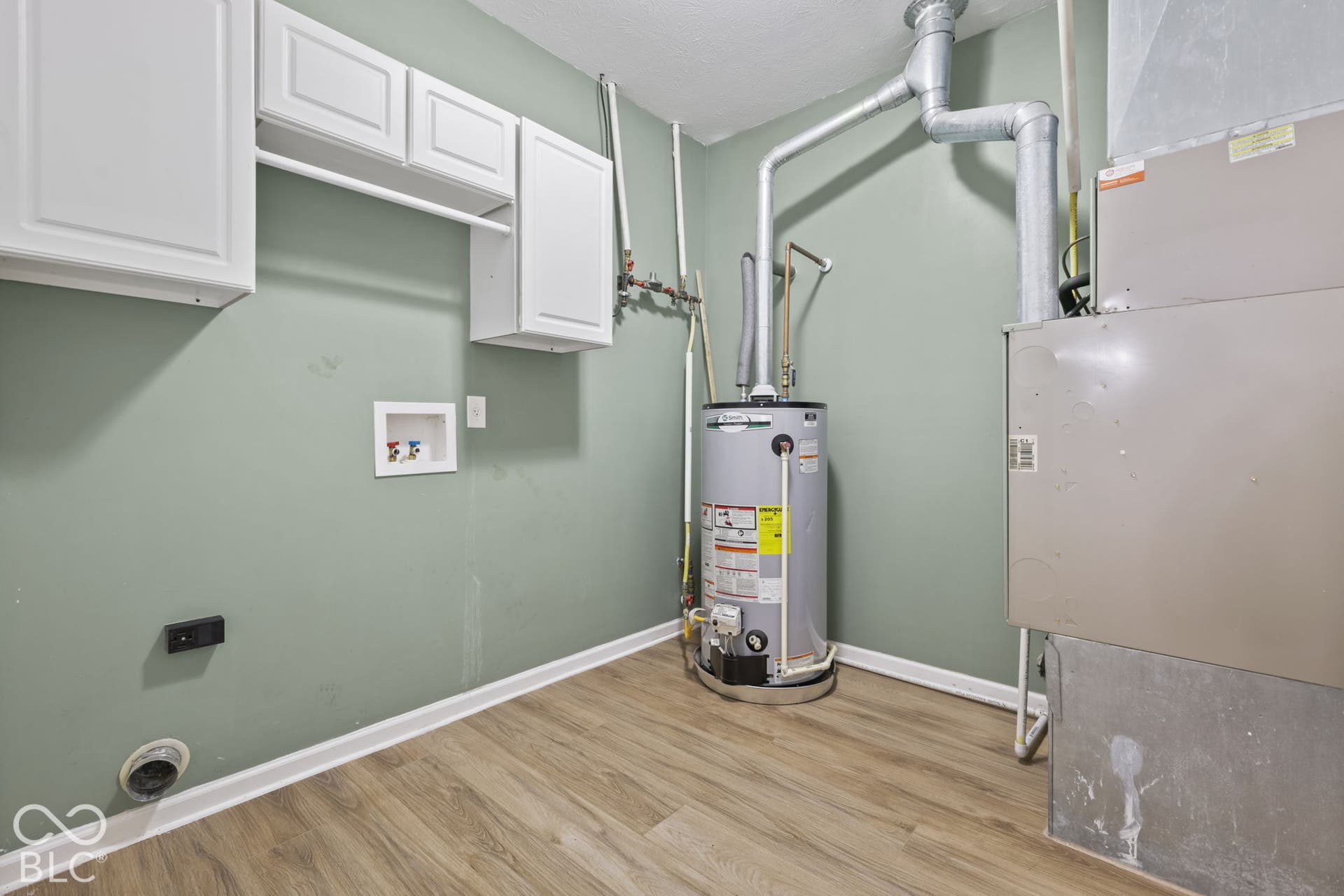 Utility area featuring wood-finish flooring, white wall-mounted cabinetry, a water heater, and an integrated climate control system