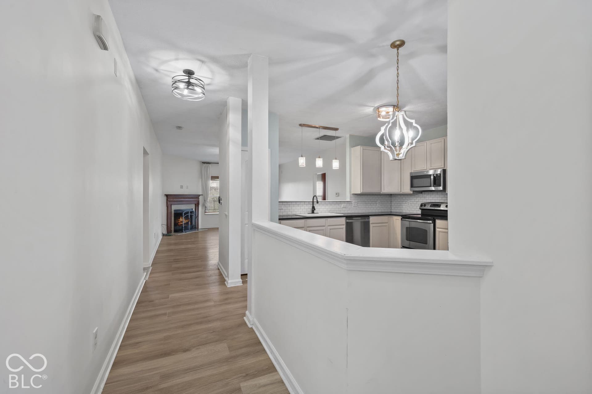 Kitchen featuring light-toned cabinetry, stainless steel appliances, and a pass-through counter, with wood-finish flooring and a fireplace with a decorative mantel visible in the distance