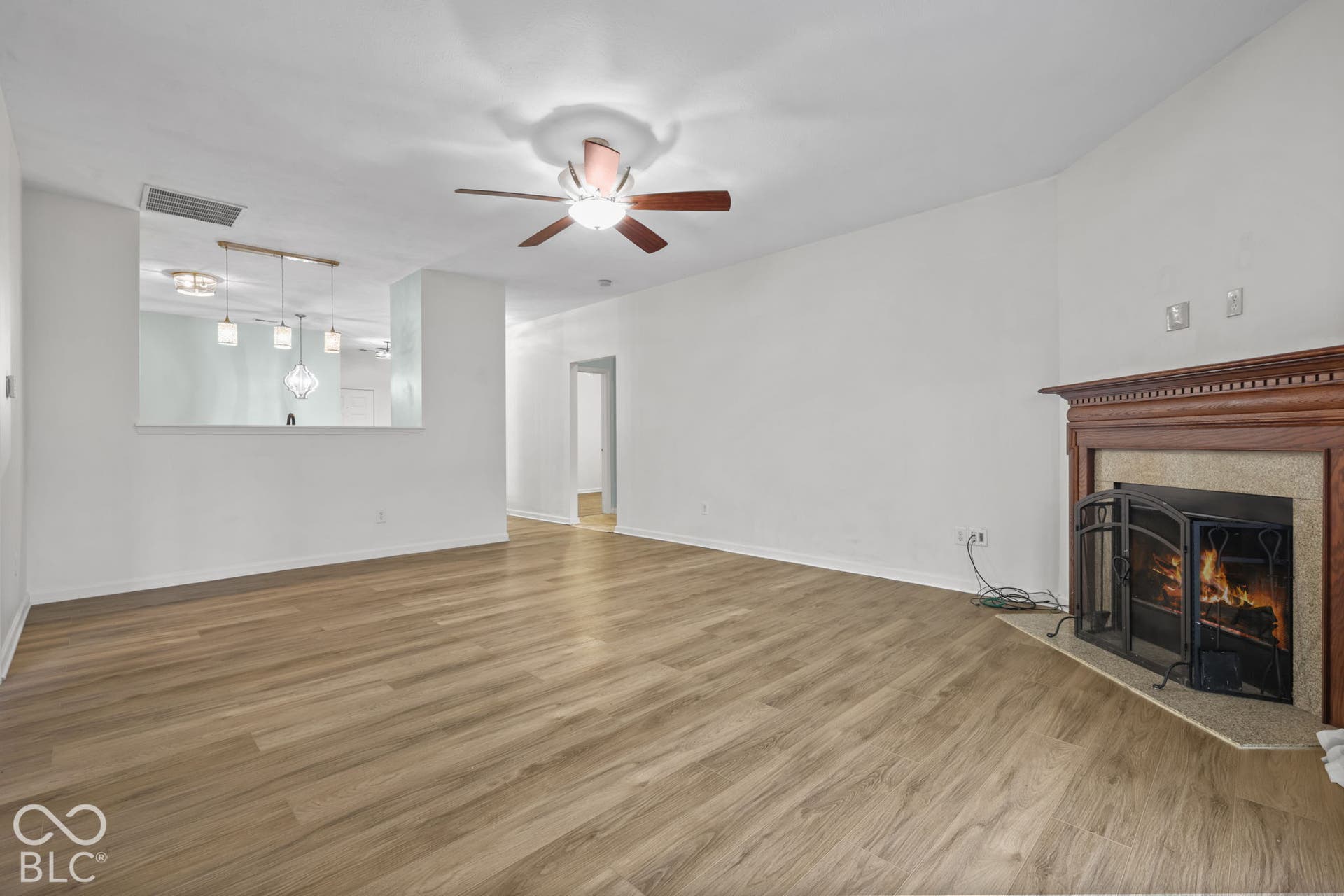 Living area featuring wood-finish flooring, a wood-mantel fireplace, a ceiling fan, and a pass-through opening