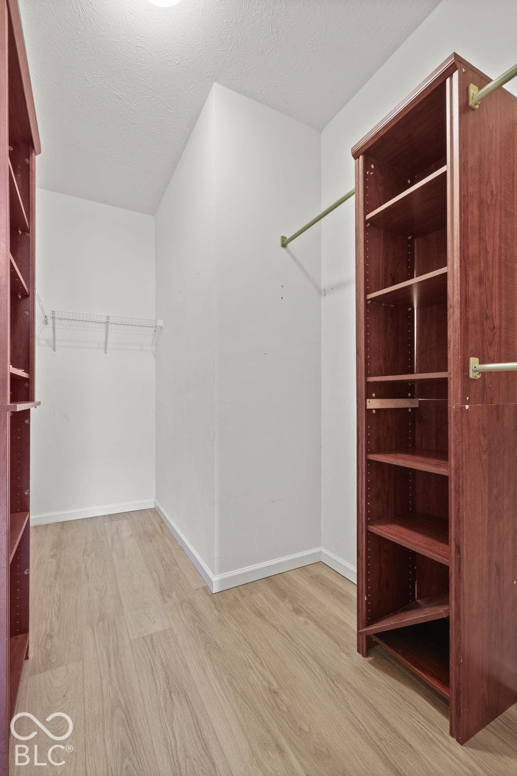 Walk-in closet featuring wood-finish flooring, built-in shelving towers, and metal hanging rods