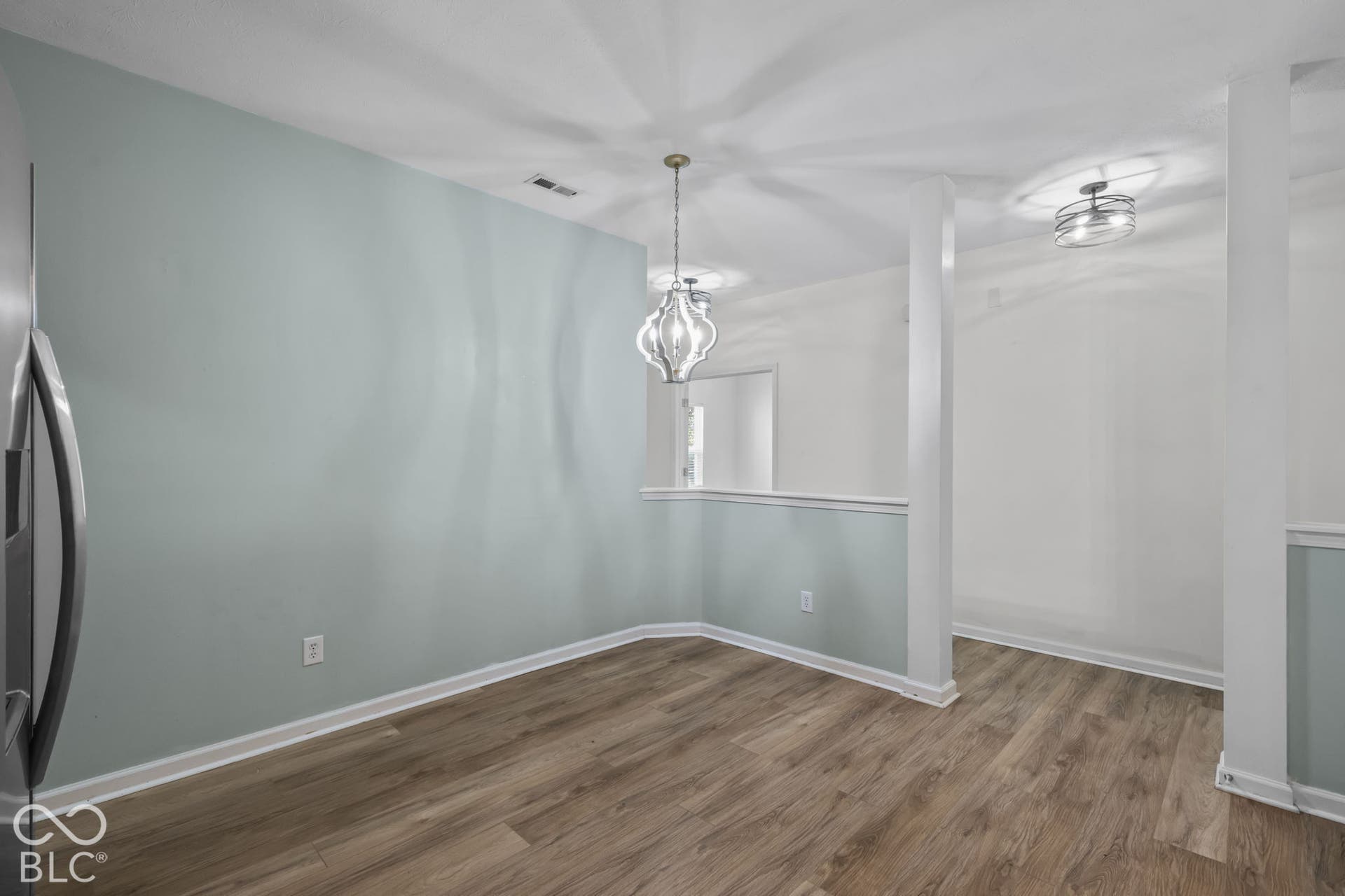 Interior space featuring wood-finish flooring, two decorative pendant light fixtures, and structural support columns with partial-height walls