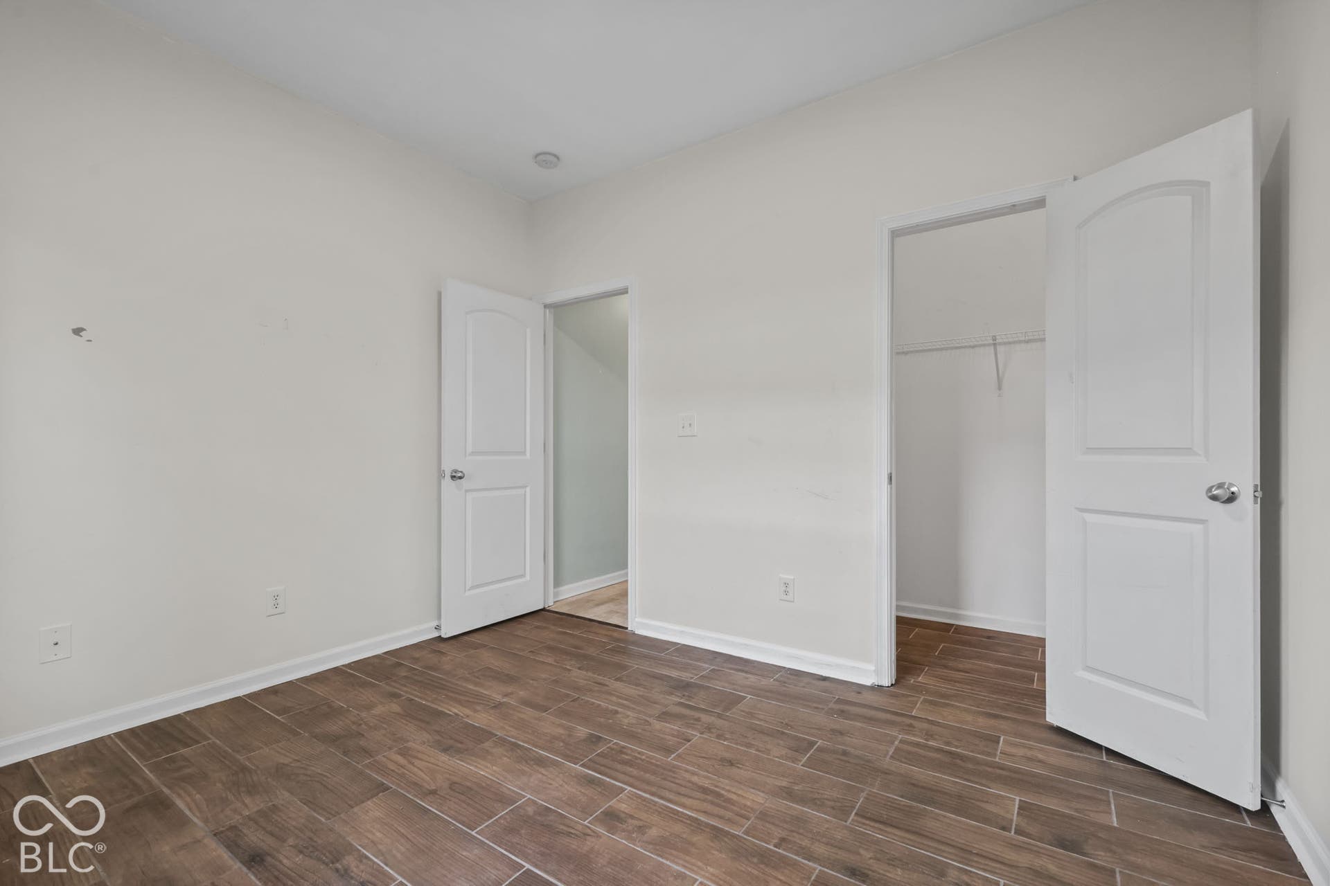 Interior room featuring wood-finish flooring, two-panel interior doors with brushed nickel hardware, and a walk-in closet with built-in shelving
