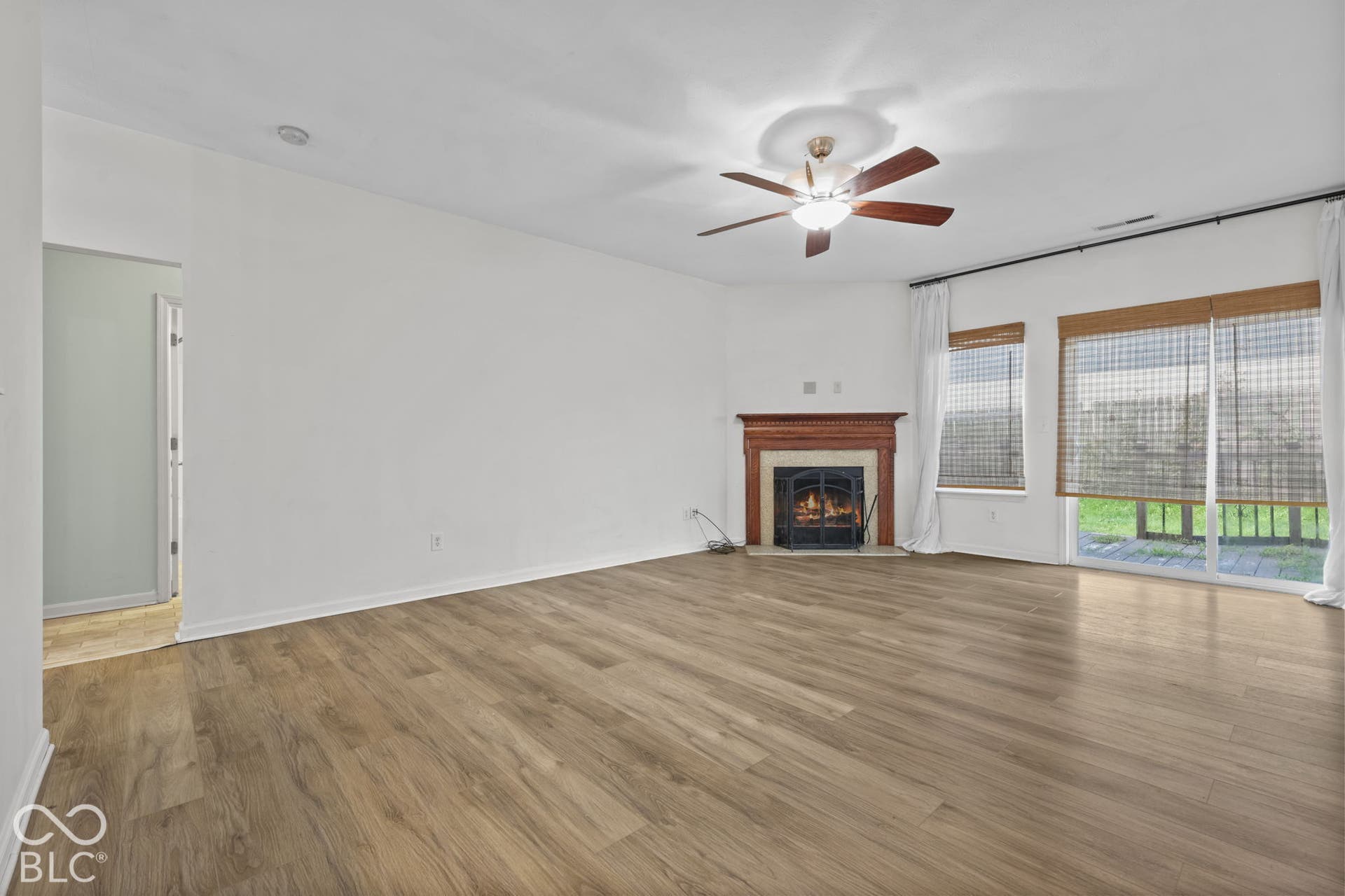 Wood-finish flooring throughout, fireplace with a decorative mantel, ceiling fan with light fixture, and sliding glass doors with exterior access