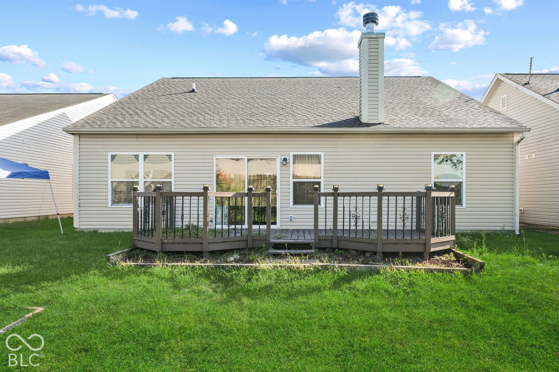 Rear elevation featuring beige vinyl siding, a raised wood deck with balustrades, a chimney, and a sliding glass door