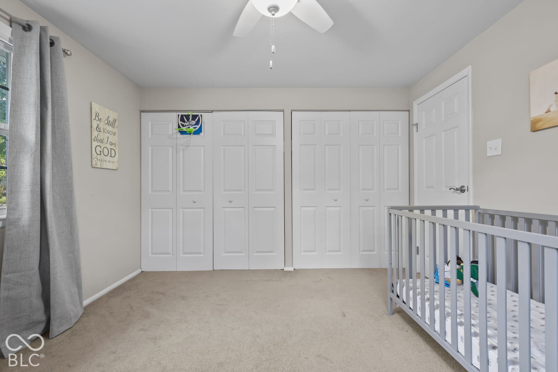 Neutral interior with wall-to-wall carpeting, dual bi-fold closet doors, and a ceiling-mounted light fixture with fan