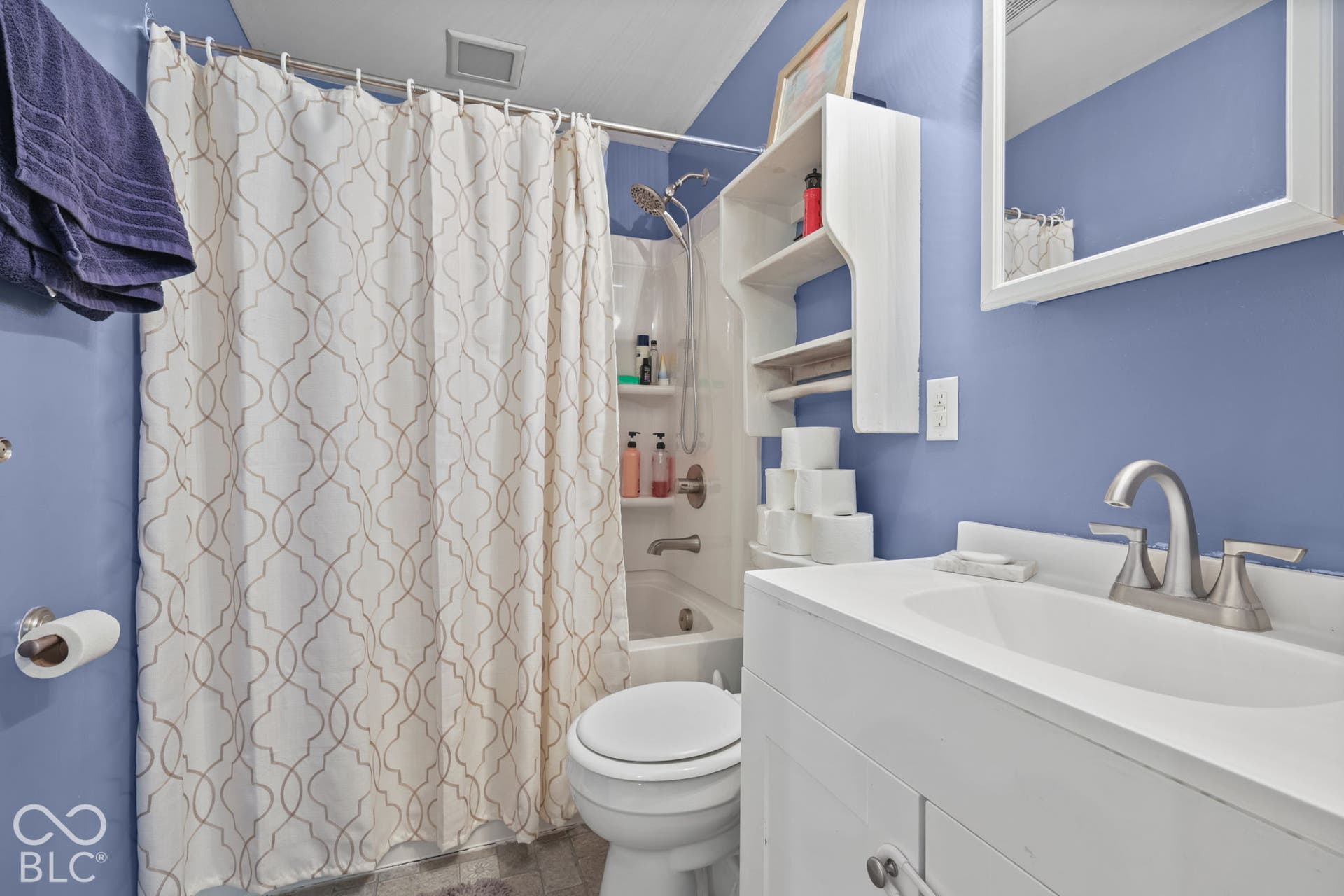 Bathroom featuring a white vanity cabinet with a integrated sink, brushed-nickel widespread faucet, wall-mounted storage shelving, and a tub-shower combination with built-in niches