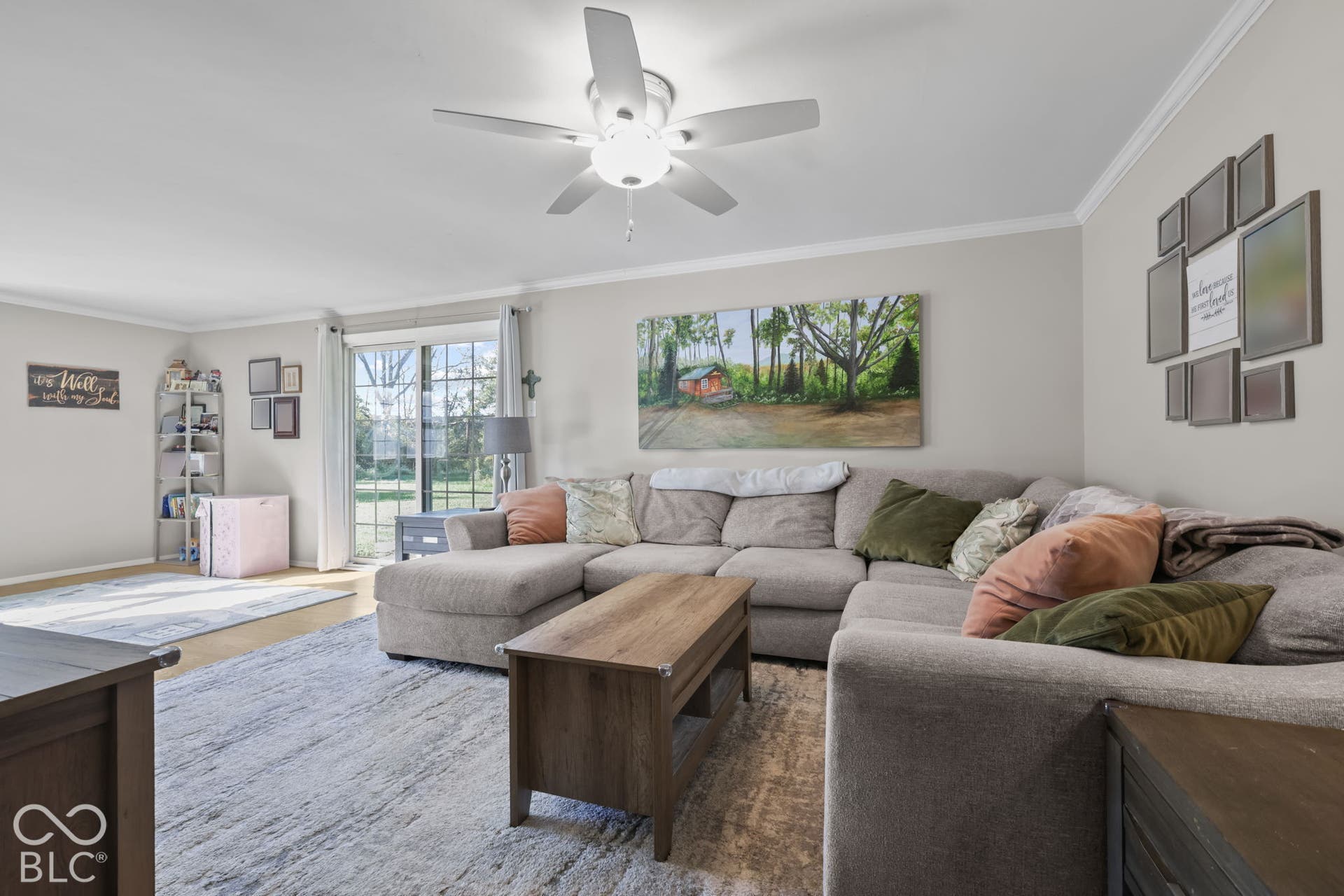 Living area featuring light-toned interior paint, crown molding, a central ceiling fan with integrated lighting, and sliding glass doors