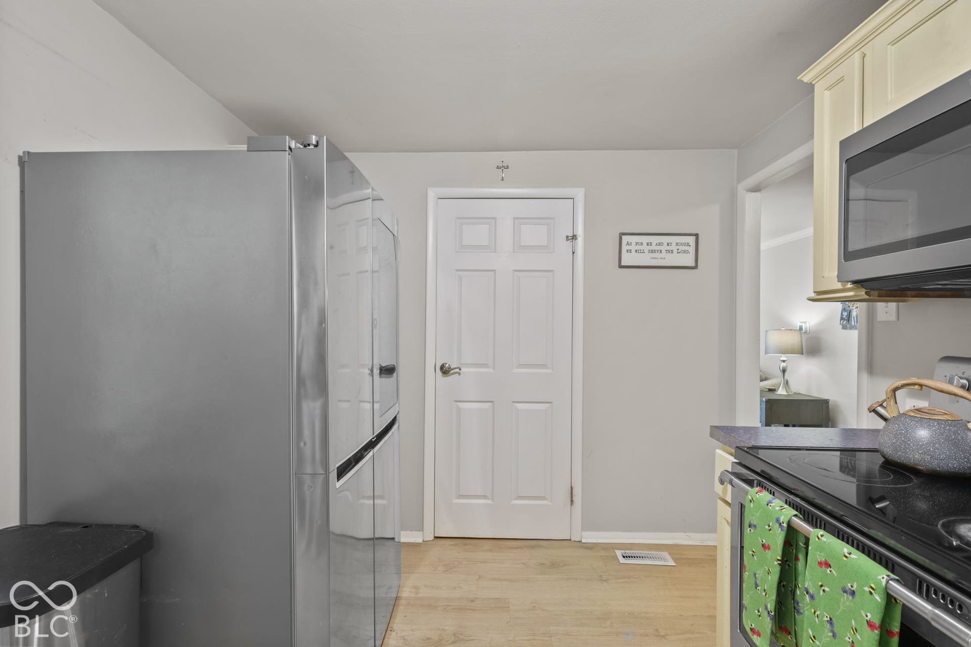 Stainless steel side-by-side refrigerator, over-the-range microwave, wood-finish flooring, and white six-panel interior door