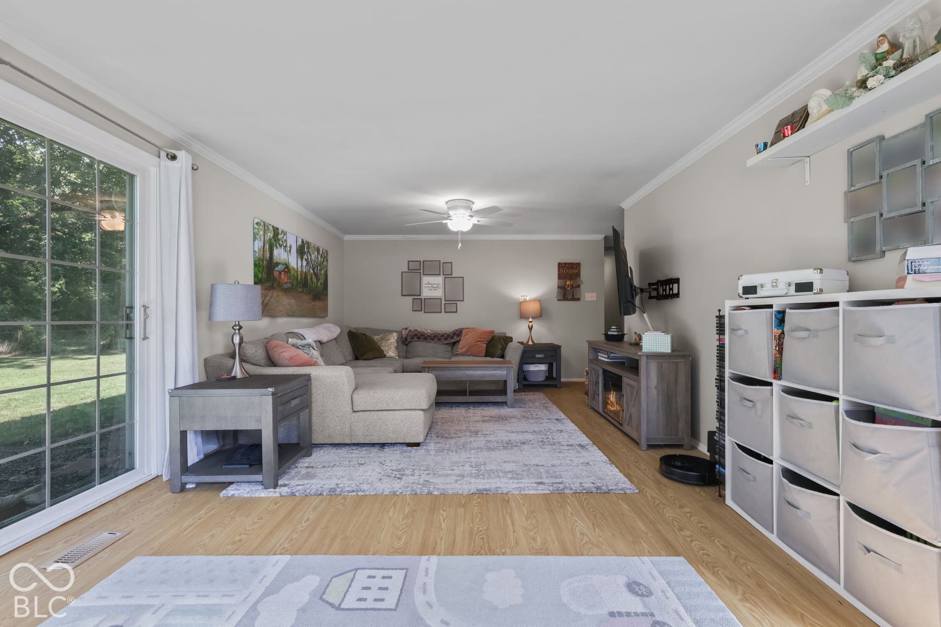Living area featuring wood-finish flooring, crown molding, a central ceiling fan with integrated lighting, and a sliding glass door