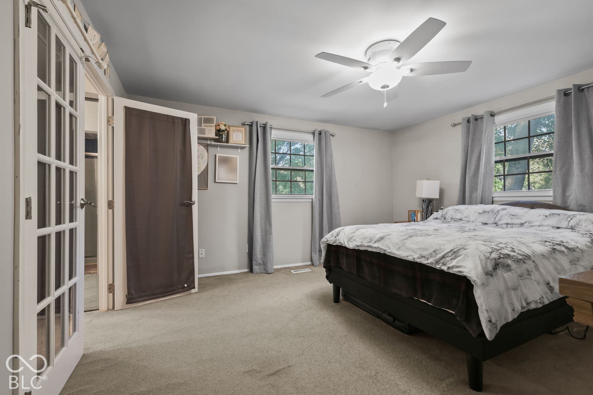 Room featuring neutral carpeting, a ceiling fan with integrated lighting, dual windows with grid-patterned glass, and a white French door with glass panels