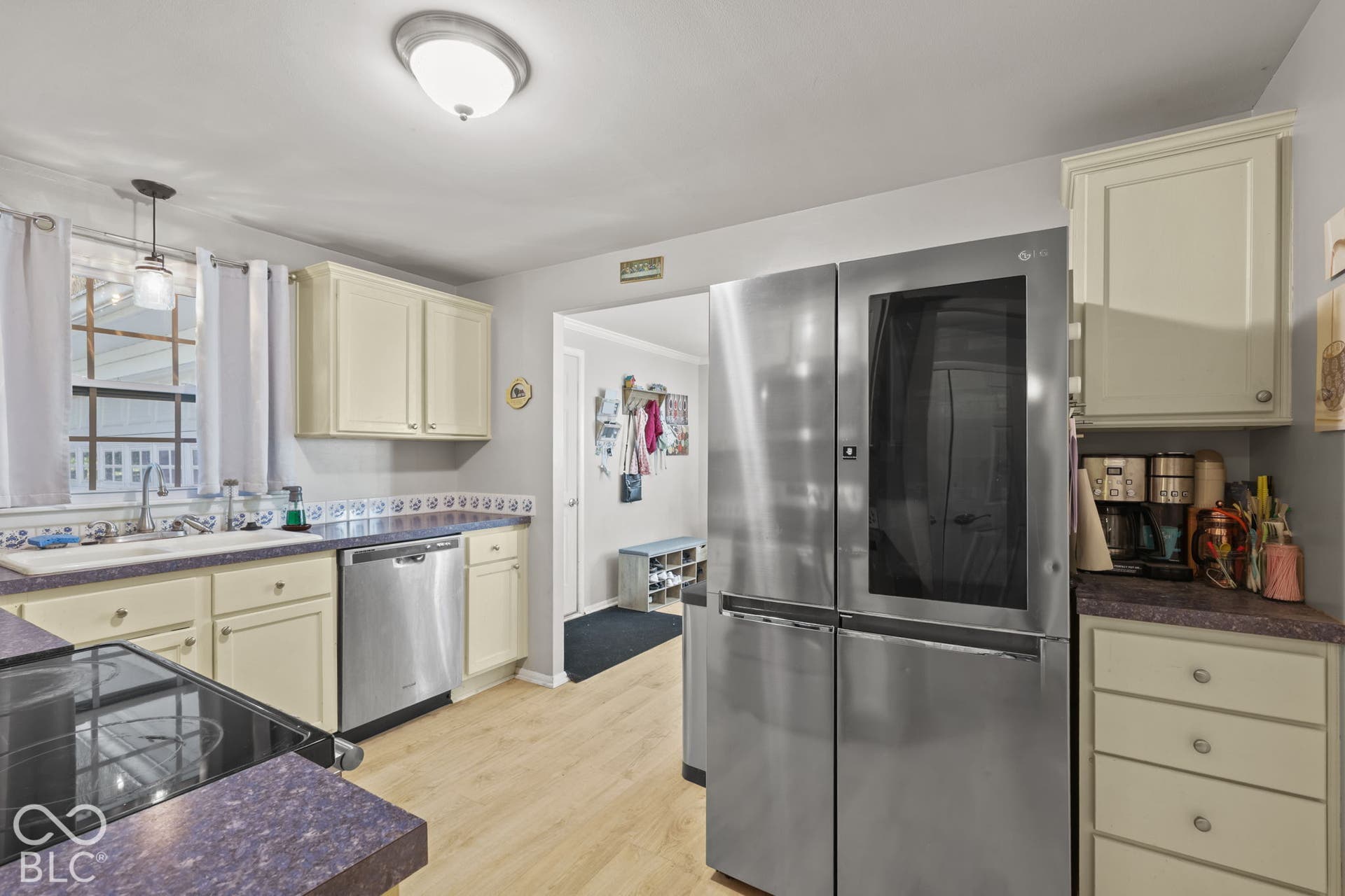 Kitchen featuring solid-surface countertops, stainless steel appliances, cream cabinetry, and wood-finish flooring