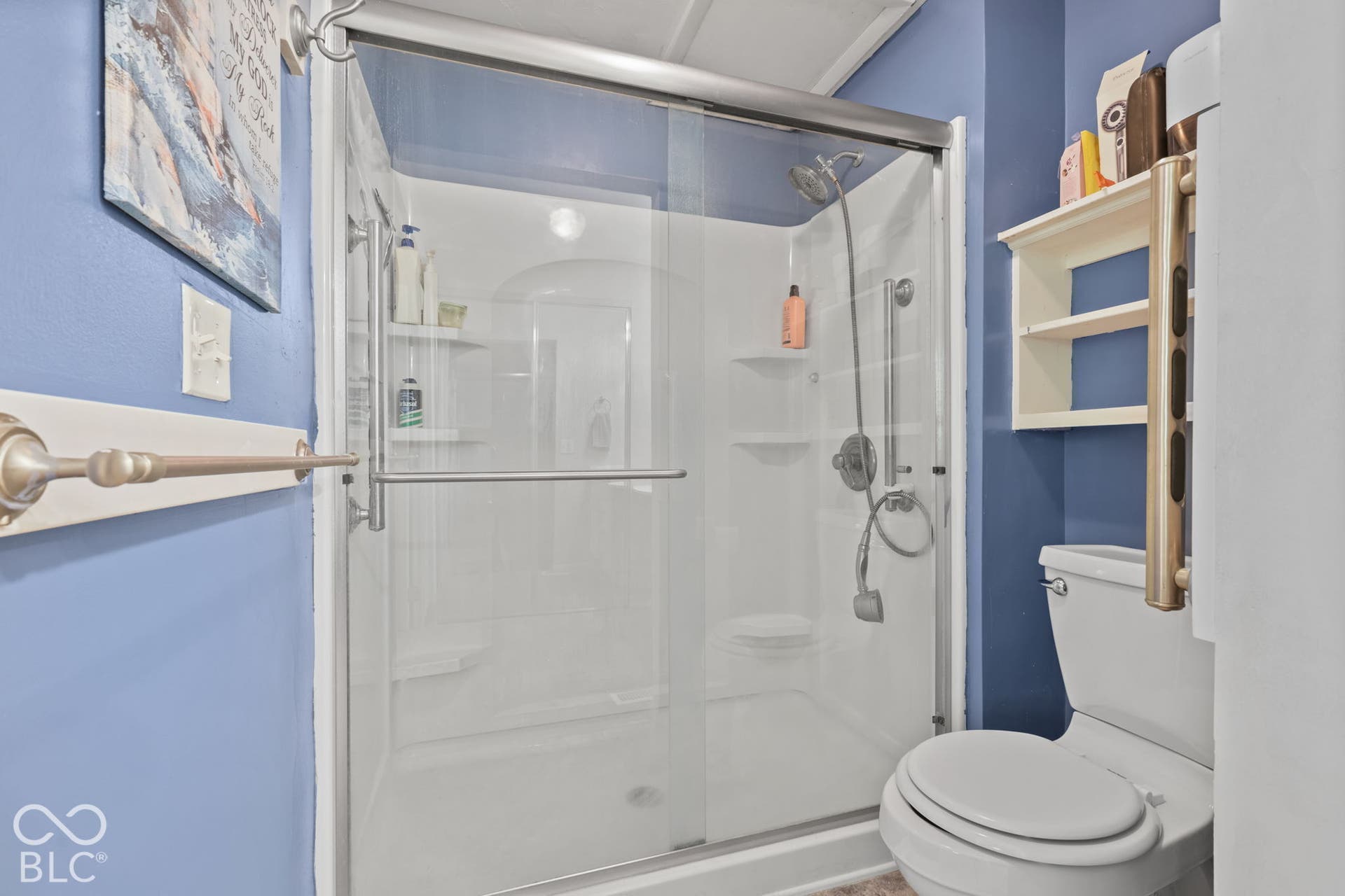Walk-in shower enclosure featuring a white acrylic surround, sliding glass doors, integrated shelving, and a handheld showerhead