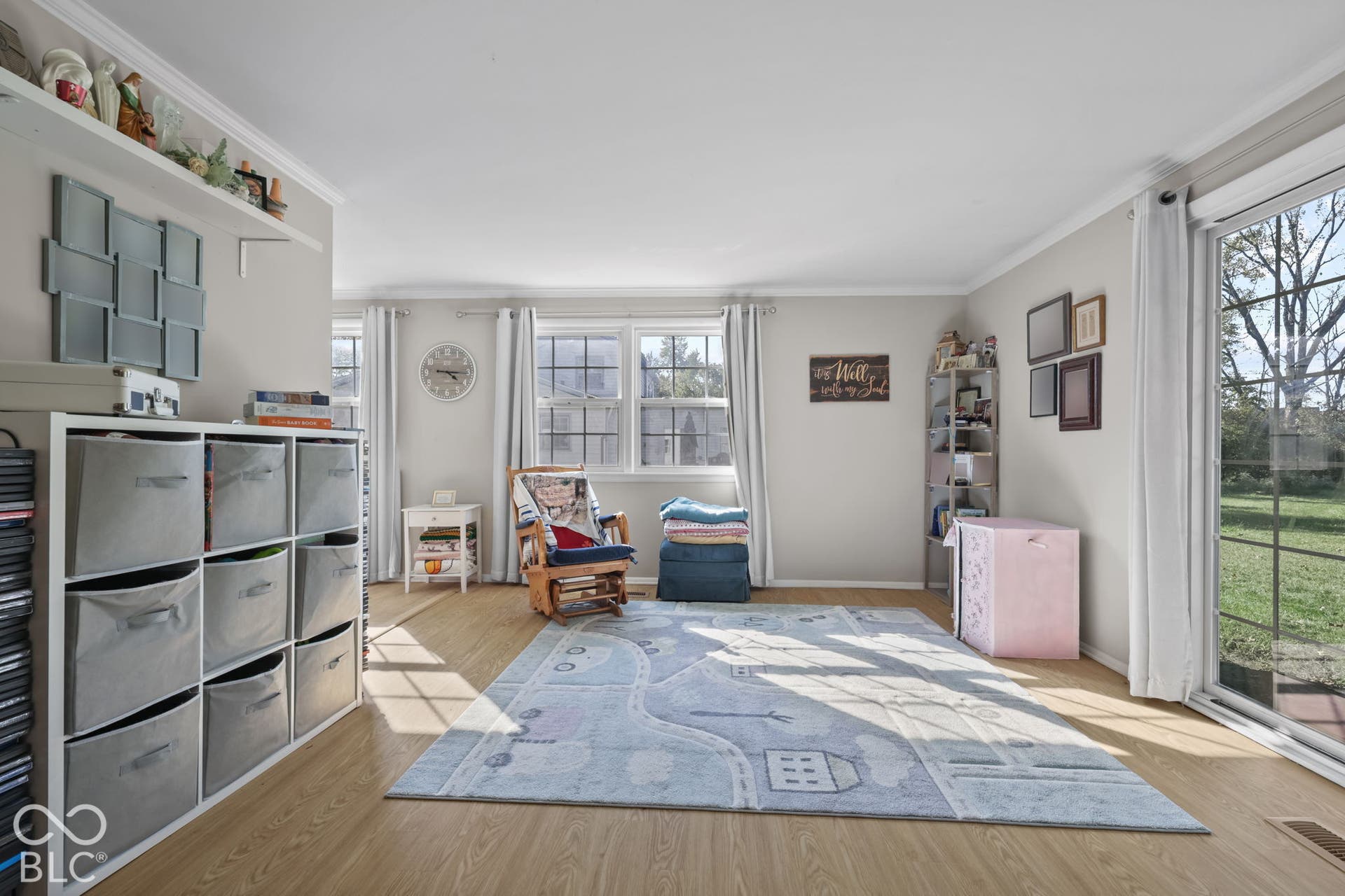 Living area featuring wood-finish flooring, crown molding, double-hung windows, and a glass sliding door providing exterior access