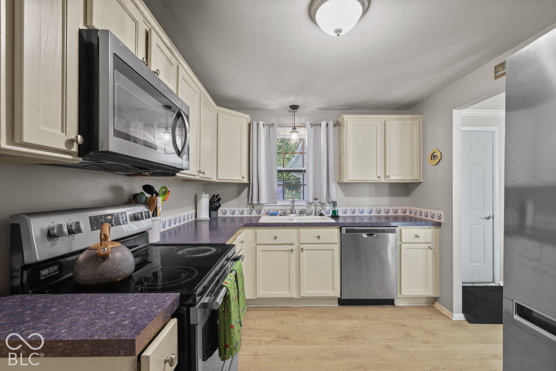 Kitchen featuring cream-colored cabinetry, stainless steel appliances, dual-basin sink, and wood-finish flooring