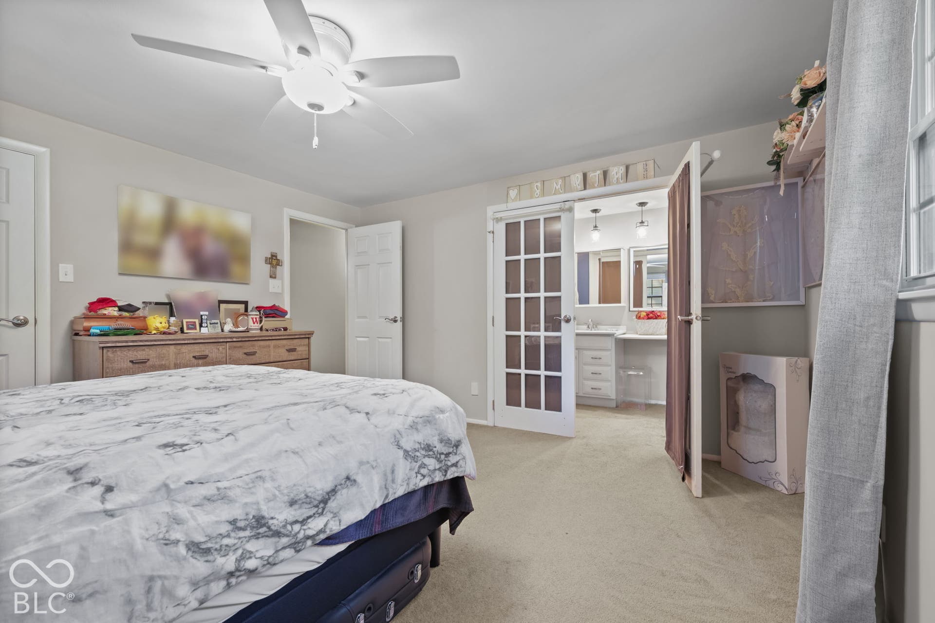 Neutral-toned room featuring neutral carpeting, a central ceiling fan with an integrated light fixture, and white French-style doors