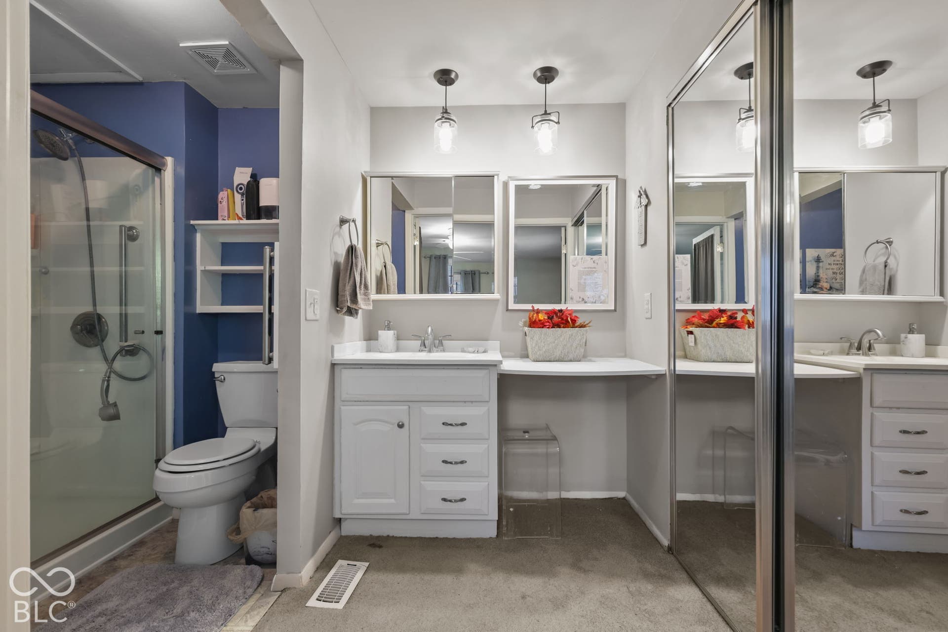 Bathroom featuring a glass-enclosed shower, dual-basin vanity with inset cabinetry, built-in vanity desk, mirrored sliding closet doors, and pendant lighting