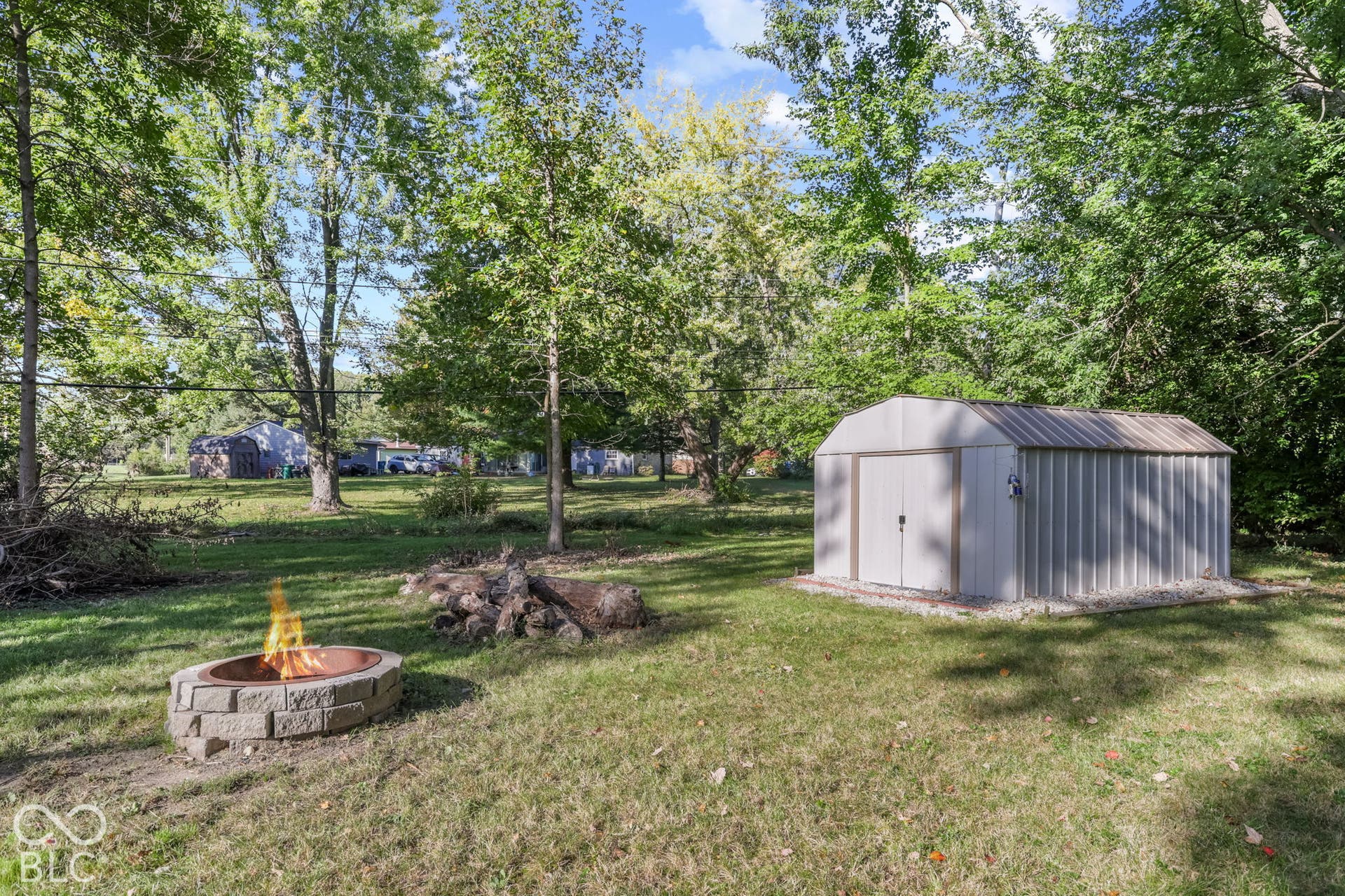 Spacious backyard featuring mature trees, a metal storage shed, and a circular stone fire pit