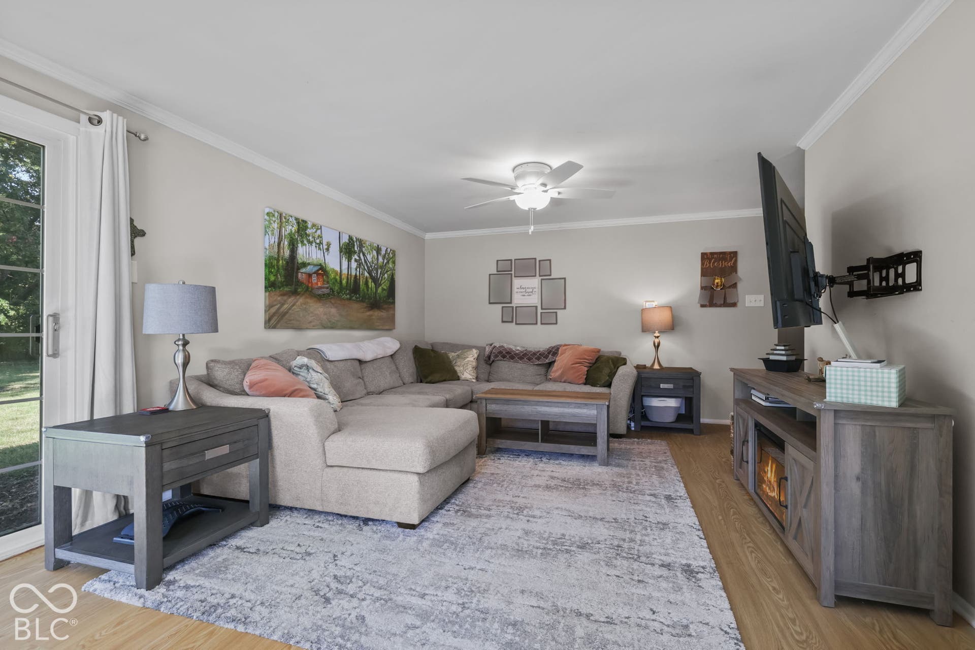 Living area featuring wood-finish flooring, crown molding, a central ceiling fan, and sliding glass door access to the exterior