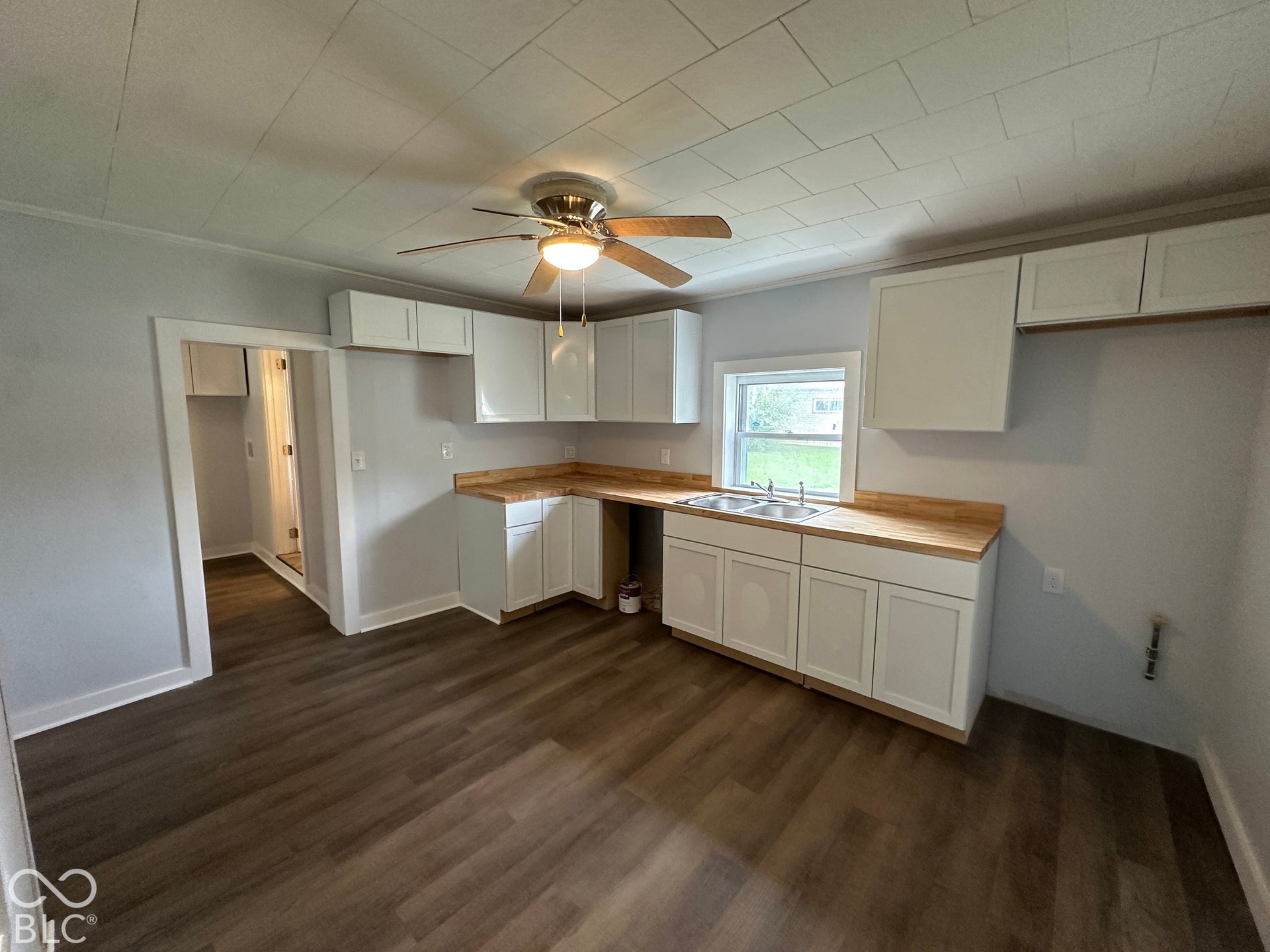 Kitchen featuring white cabinetry, wood-finish countertops, wood-finish flooring, a stainless steel double sink, and a ceiling fan with integrated lighting