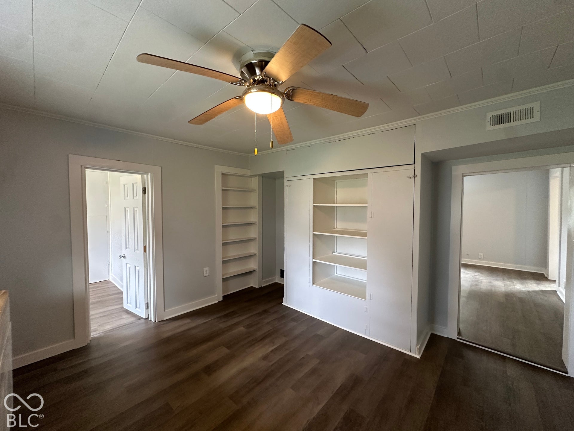 Wood-finish flooring, built-in shelving, ceiling fan with integrated lighting, and light gray wall paint