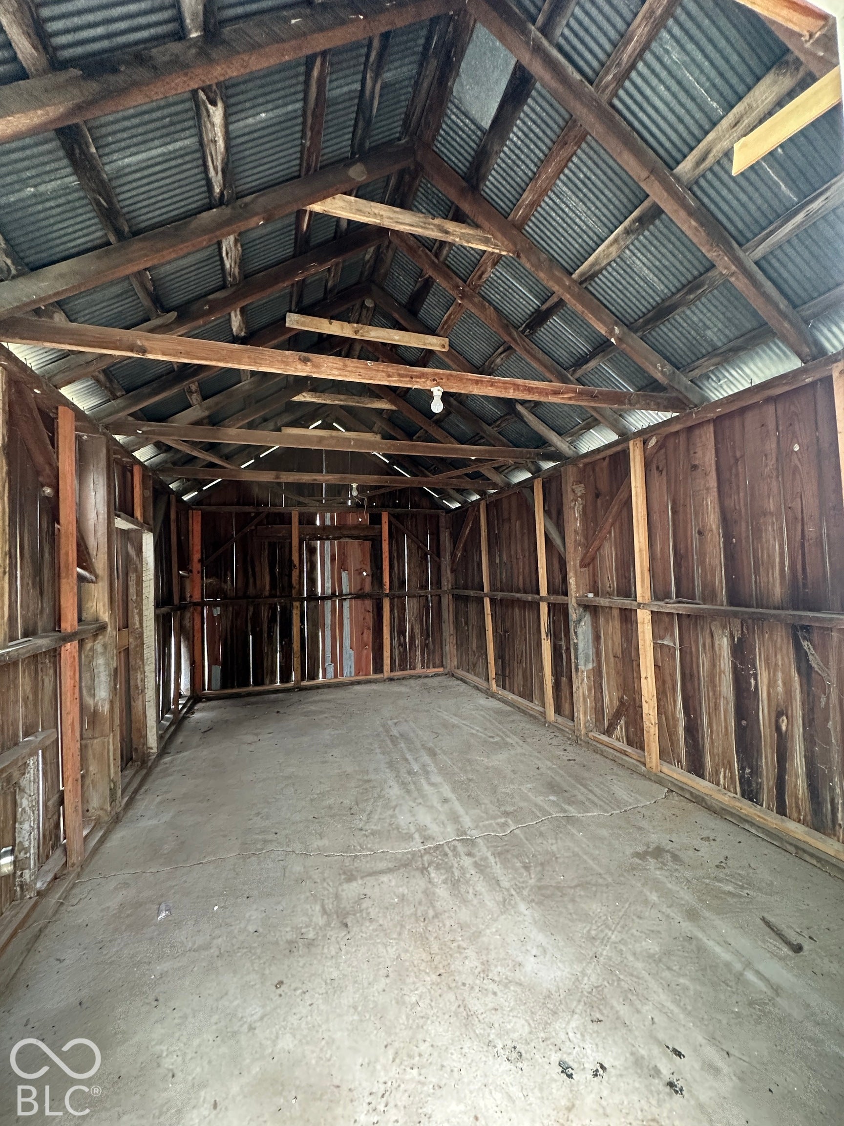 Wood-paneled interior walls, concrete flooring, and an exposed wood beam ceiling with corrugated metal roofing
