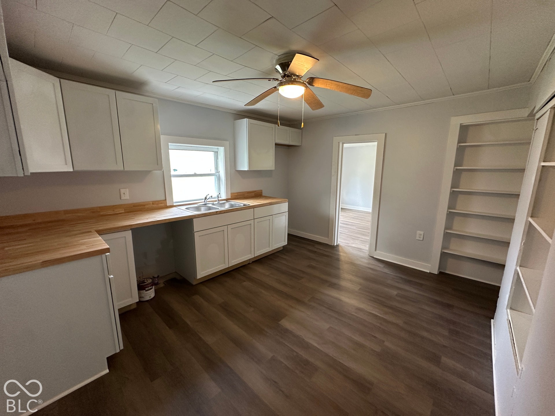 White cabinetry with wood-finish countertops, stainless steel double basin sink, and wood-finish flooring