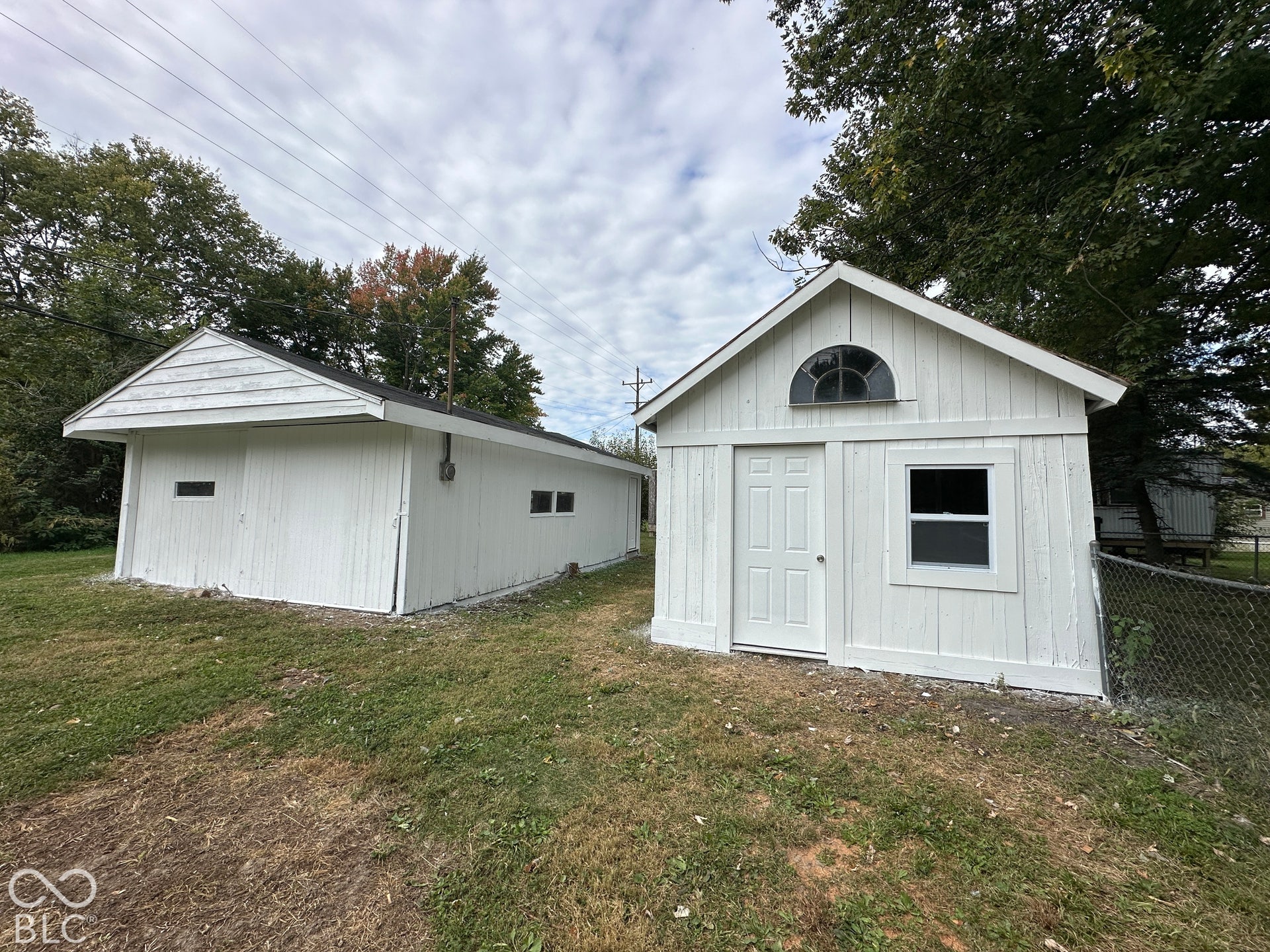 Two white outbuildings featuring pitched roofs and a grass-covered ground
