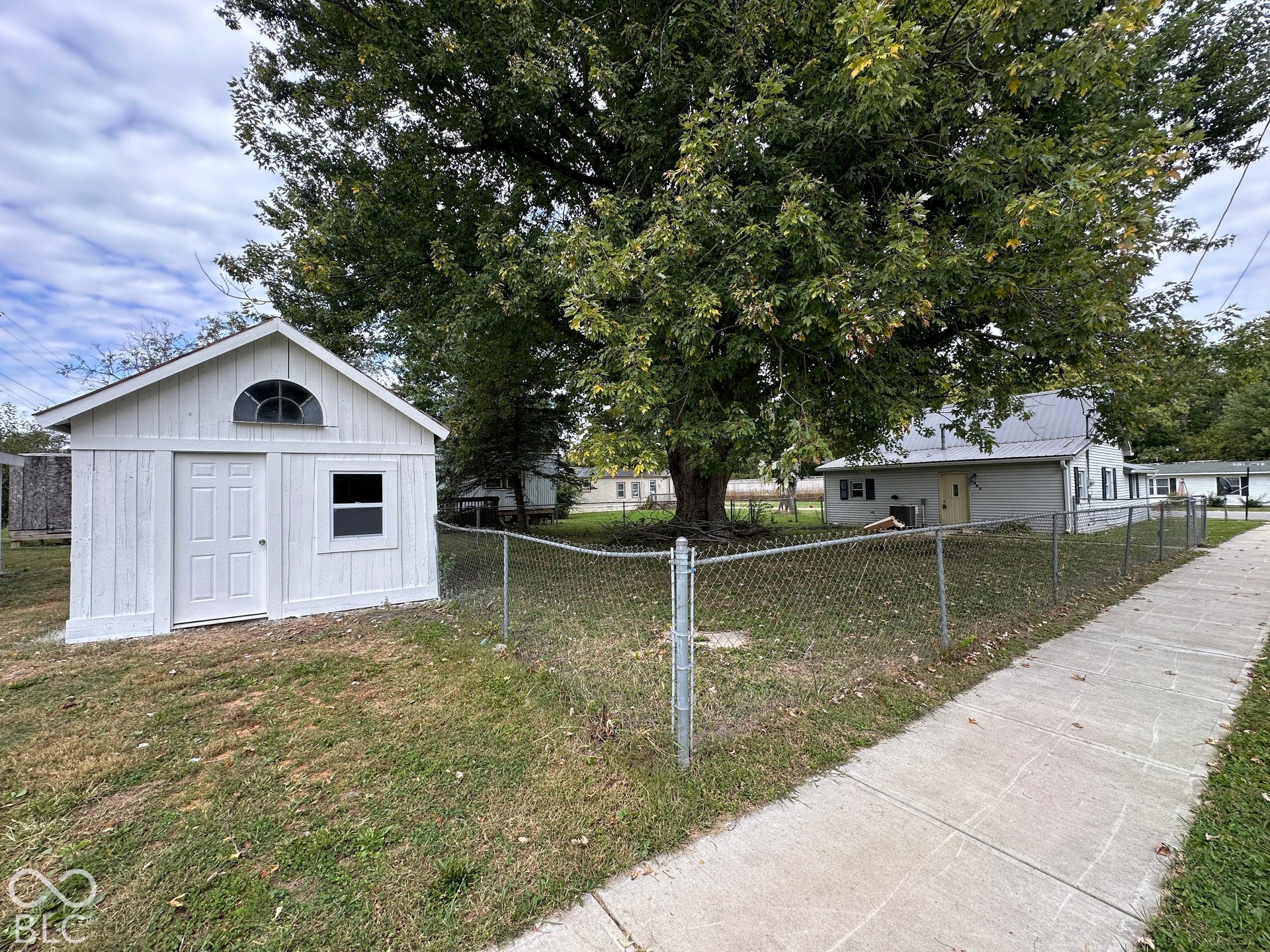 Detached white shed with an arched transom window and a chain-link fence enclosing the yard
